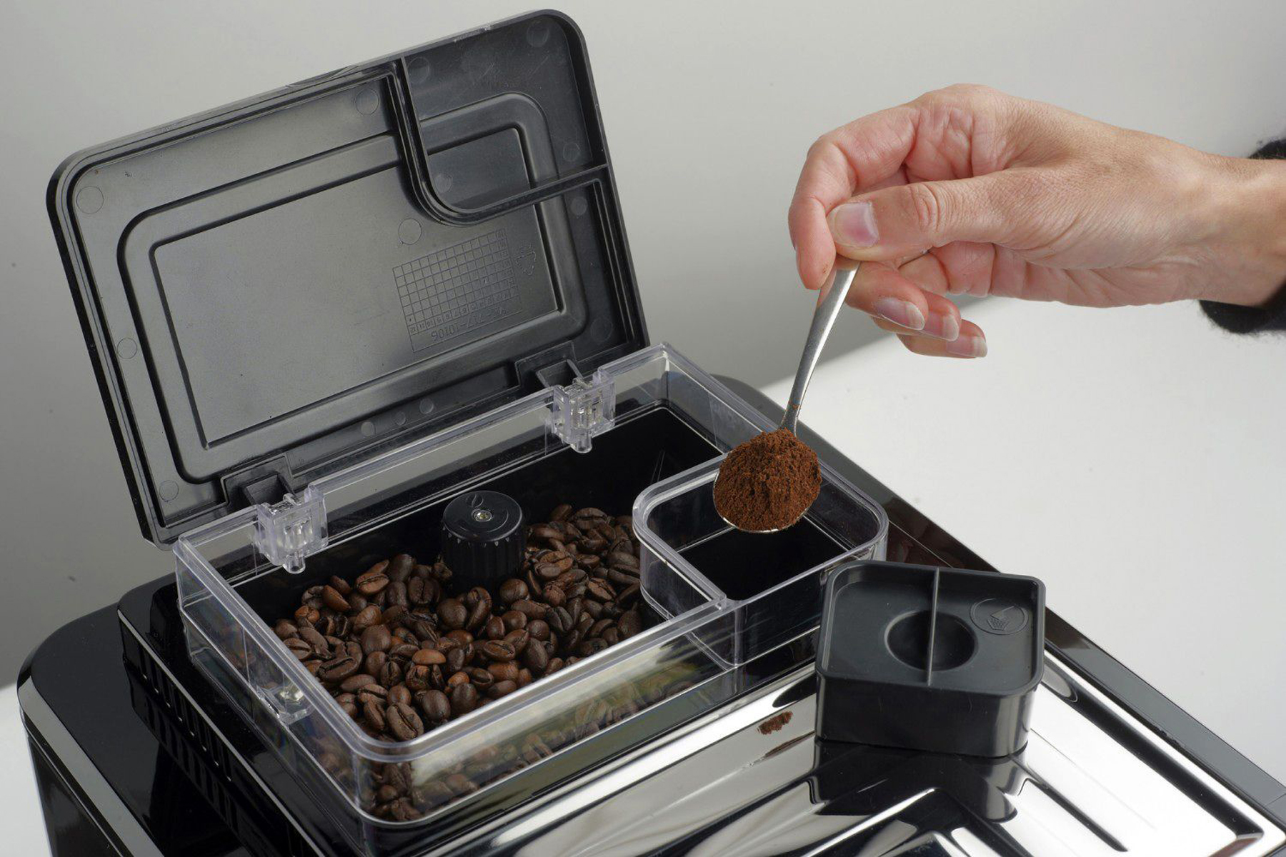 Osoba dodaje zmieloną kawę do ekspresu za pomocą łyżki. Białe tło.