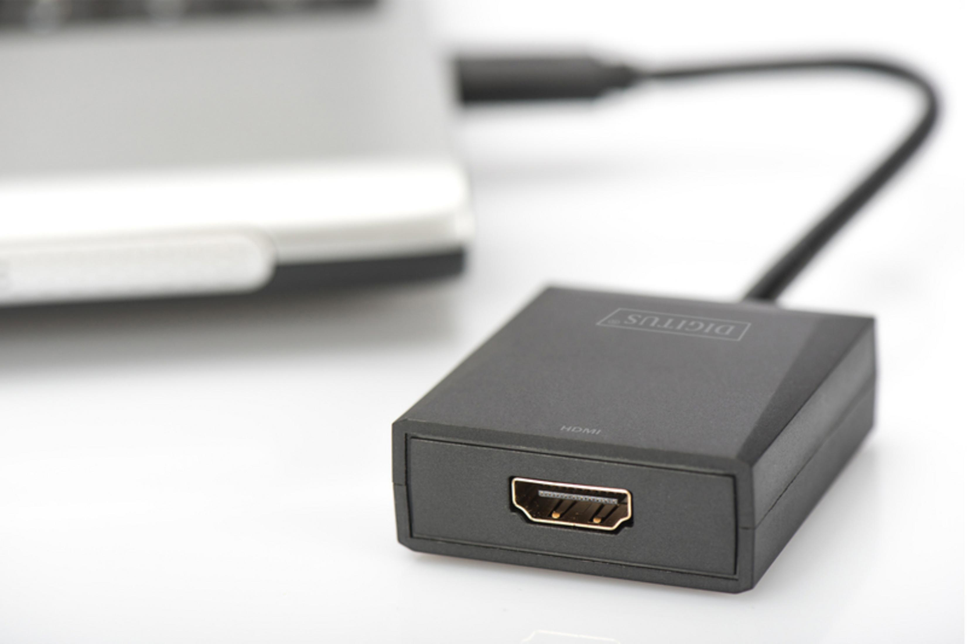 Un adaptador HDMI negro conectado a un portátil sobre un fondo blanco.
