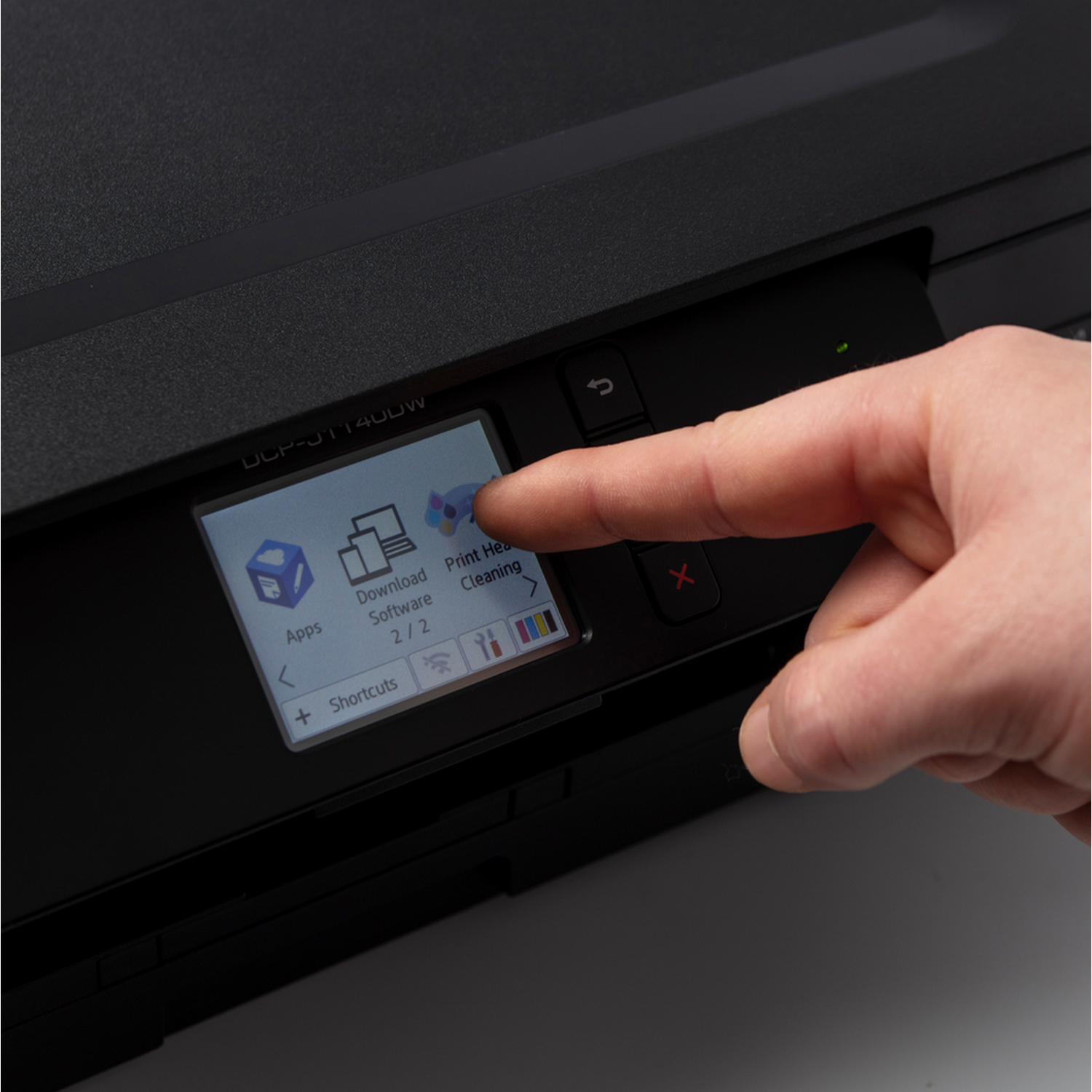 Ręka osoby wskazująca na ekran drukarki wyświetlający aplikacje i opcje oprogramowania.