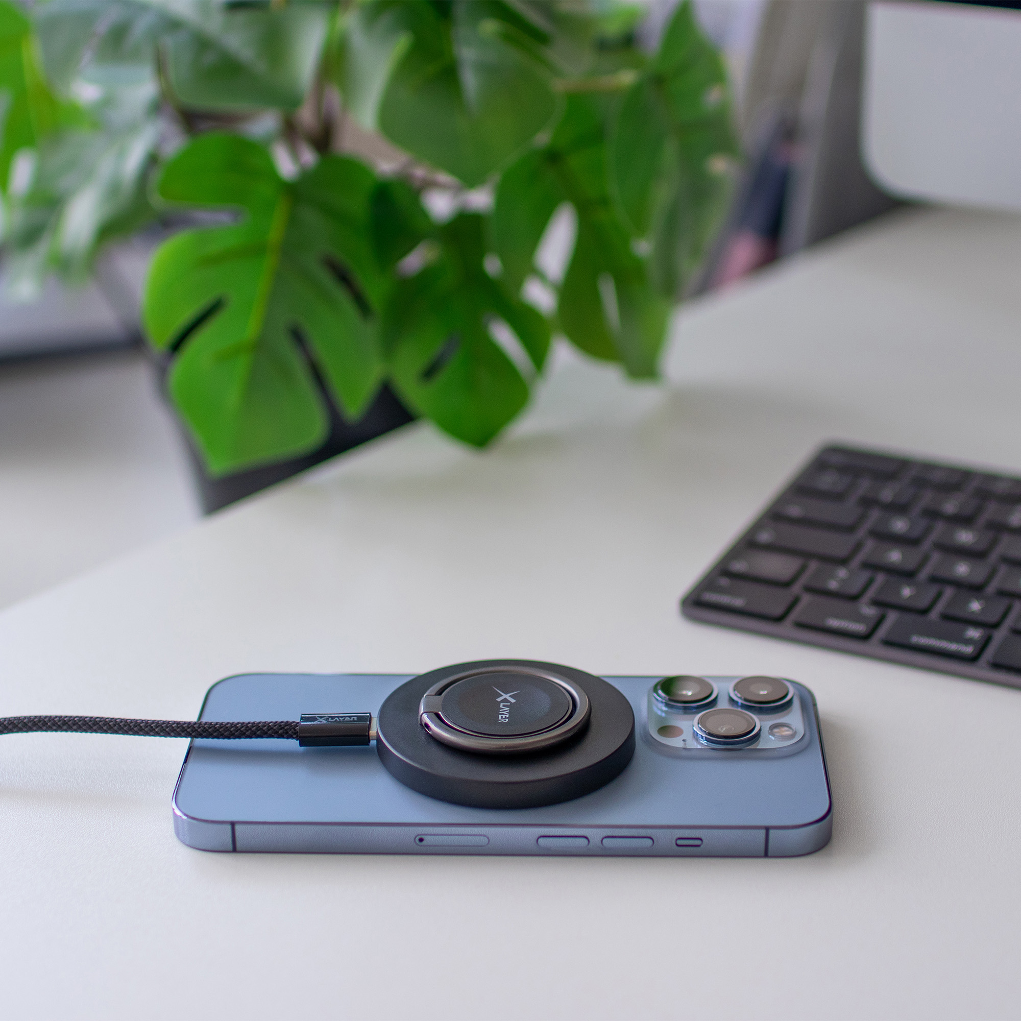 Ein Telefon auf einem weißen Schreibtisch mit einem magnetischen Ladegerät und einer Tastatur im Hintergrund.