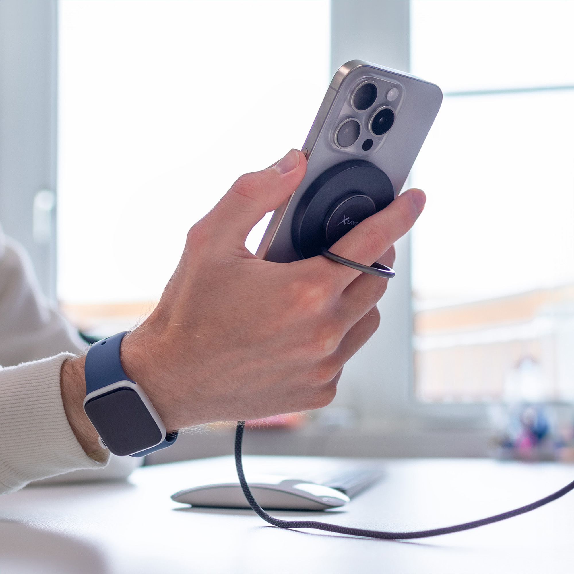Eine Person hält ein Telefon mit einem schwarzen Magnetring. Eine Smartwatch ist am Handgelenk.