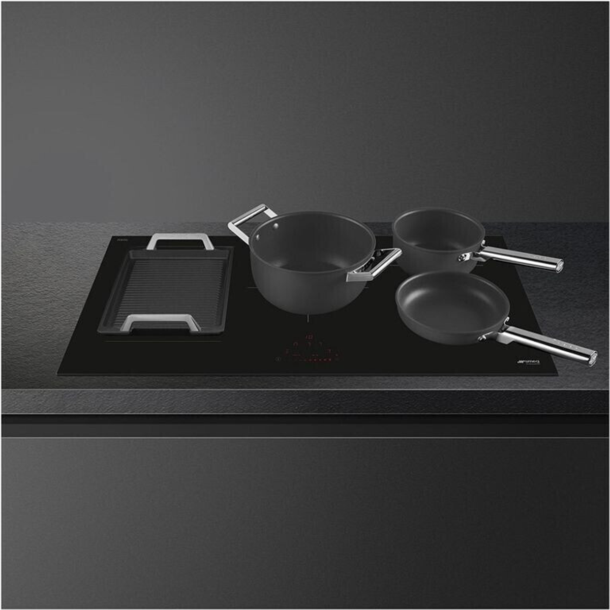 Piano cottura a induzione Smeg nero con pentole e padelle sopra, su sfondo scuro.