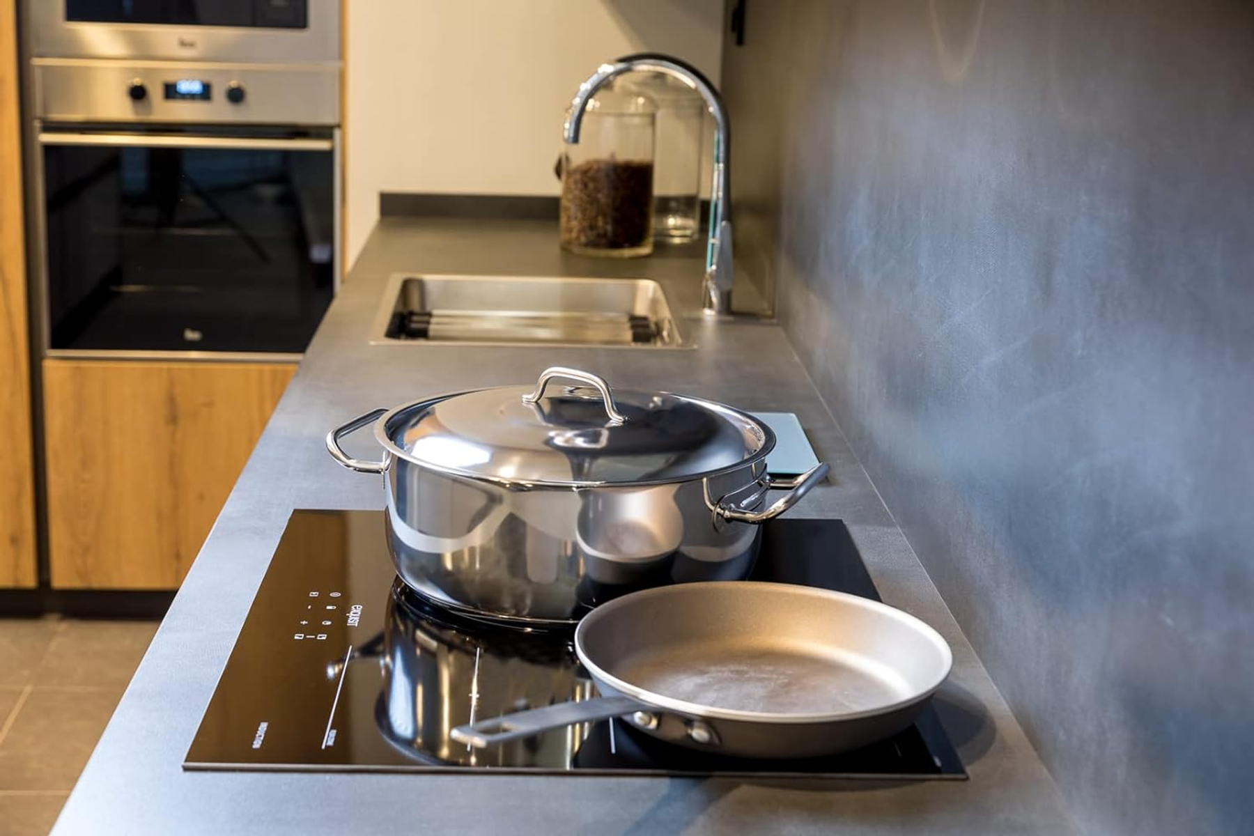 Escena de cocina con olla y sartén en una placa de inducción negra. Acero inoxidable y gris.