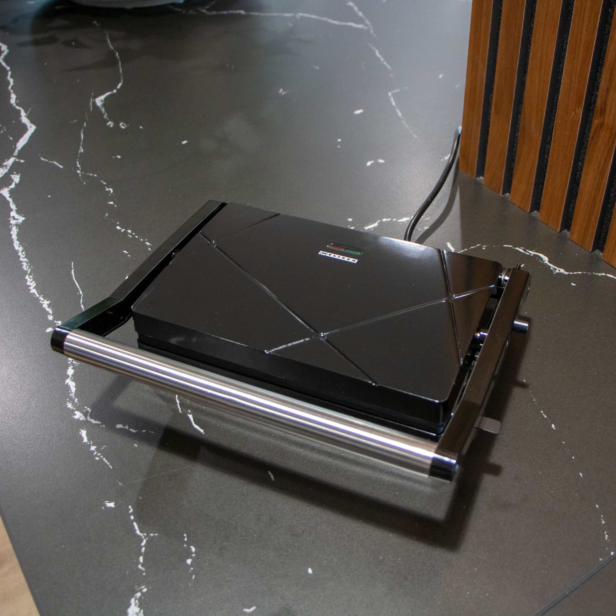 Czarna prasa do panini na ciemnym blacie, ze srebrnym uchwytem.