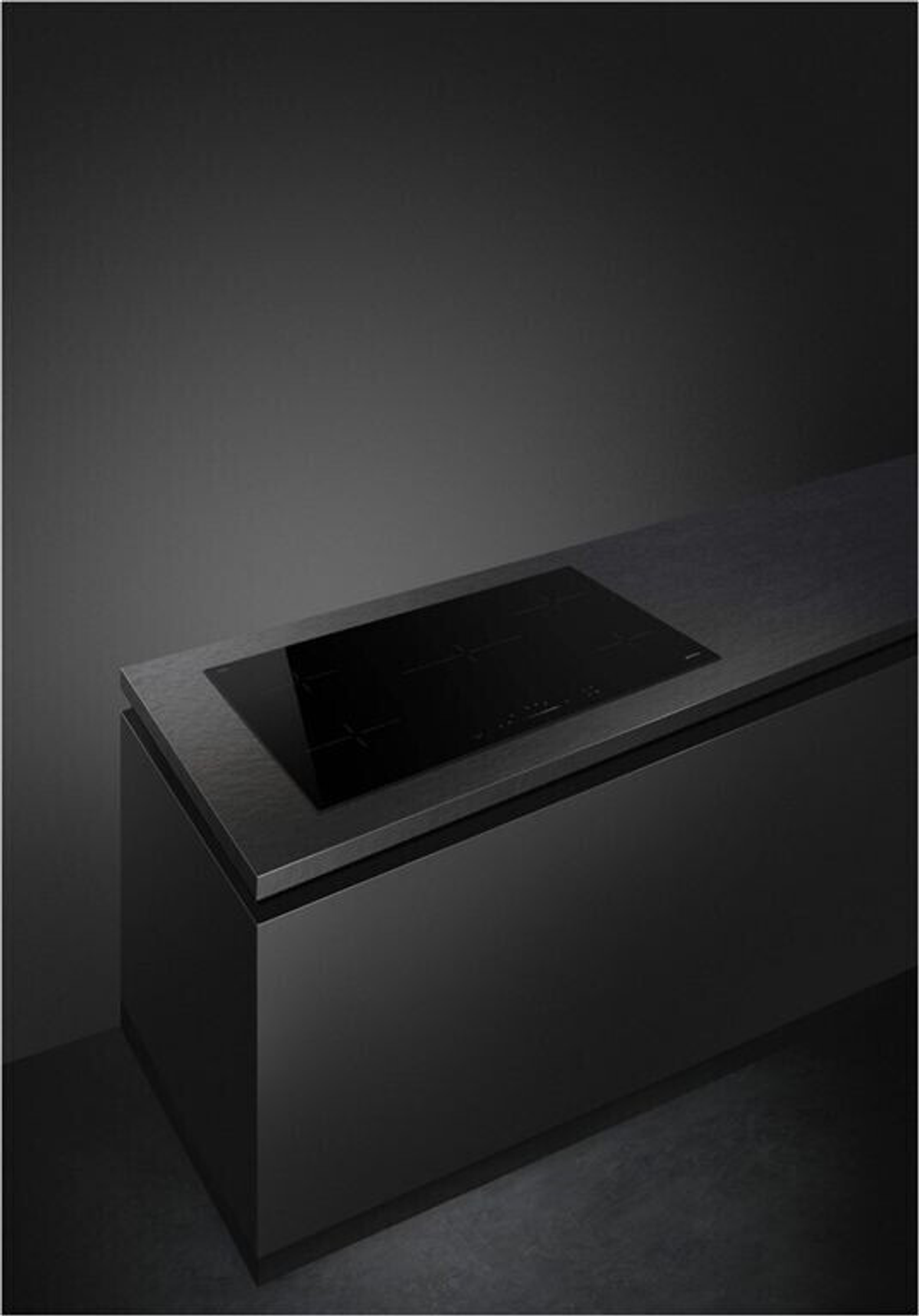 Un piano cottura nero su un piano di lavoro nero, con un muro grigio scuro sullo sfondo.