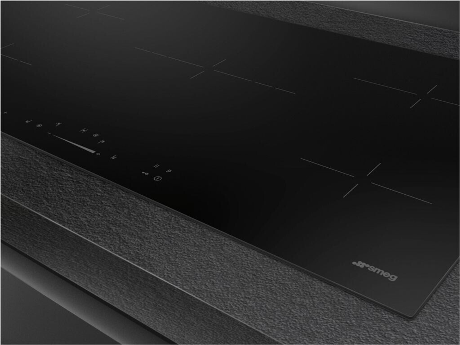 Un piano cottura a induzione nero con quattro zone cottura. Il piano è incassato in un piano di lavoro scuro e strutturato.