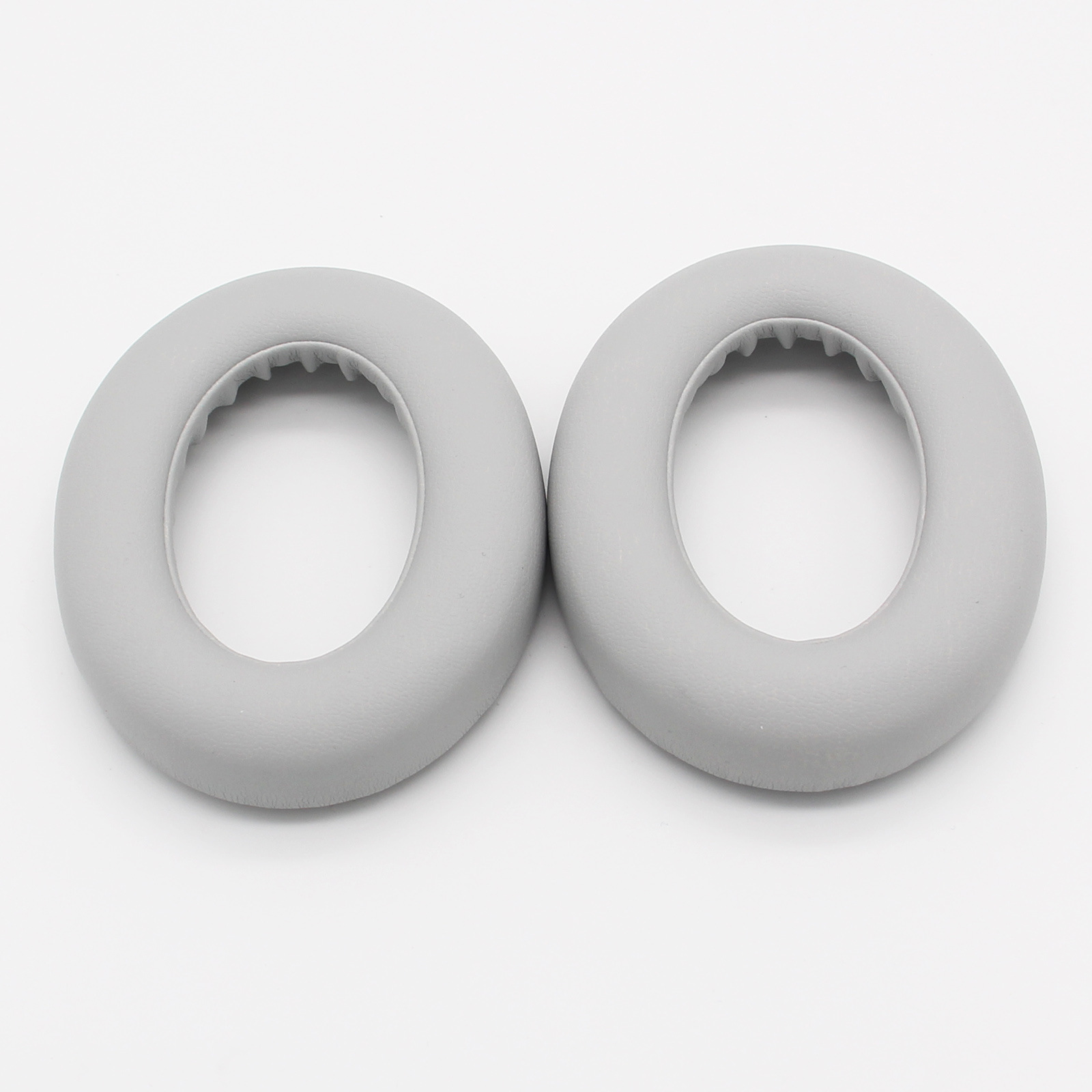 Dwie szare, okrągłe nausznice do słuchawek na białym tle. Wyglądają na miękkie i amortyzowane.