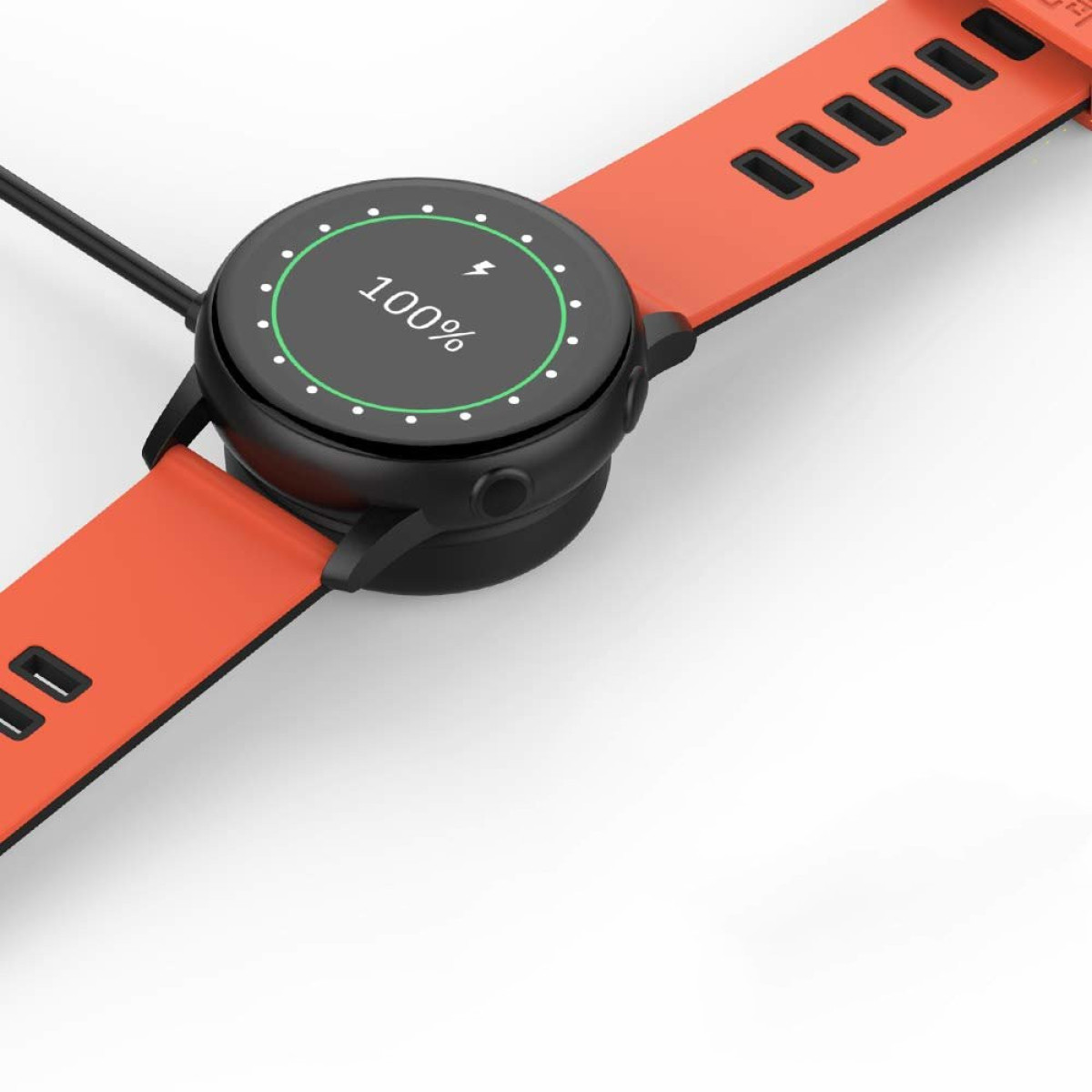 Czarny smartwatch na pomarańczowej podkładce ładującej. Zegarek pokazuje 100% naładowania.