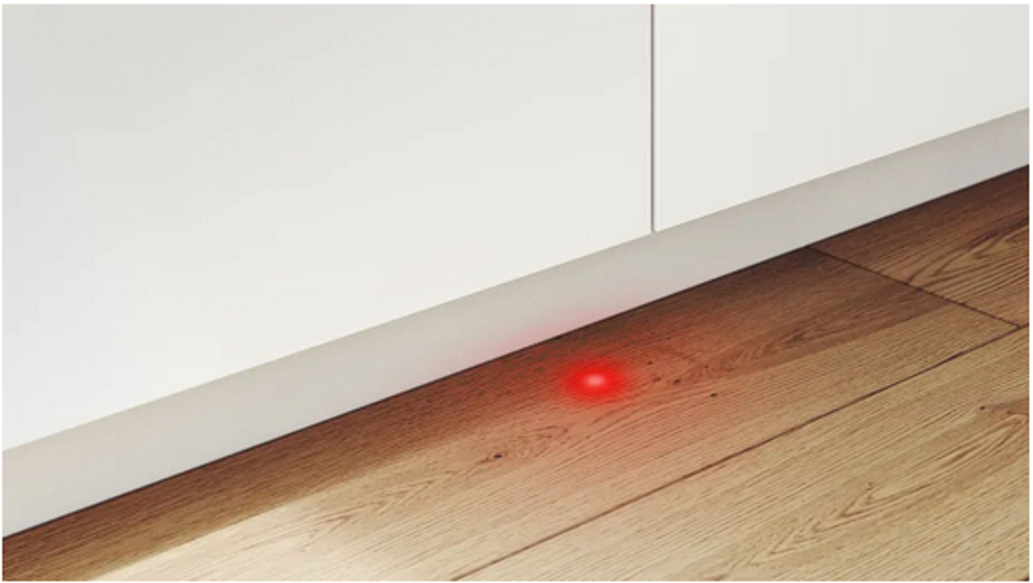 Rotes Licht auf Holzboden, in der Nähe eines weißen Schrankfußes.