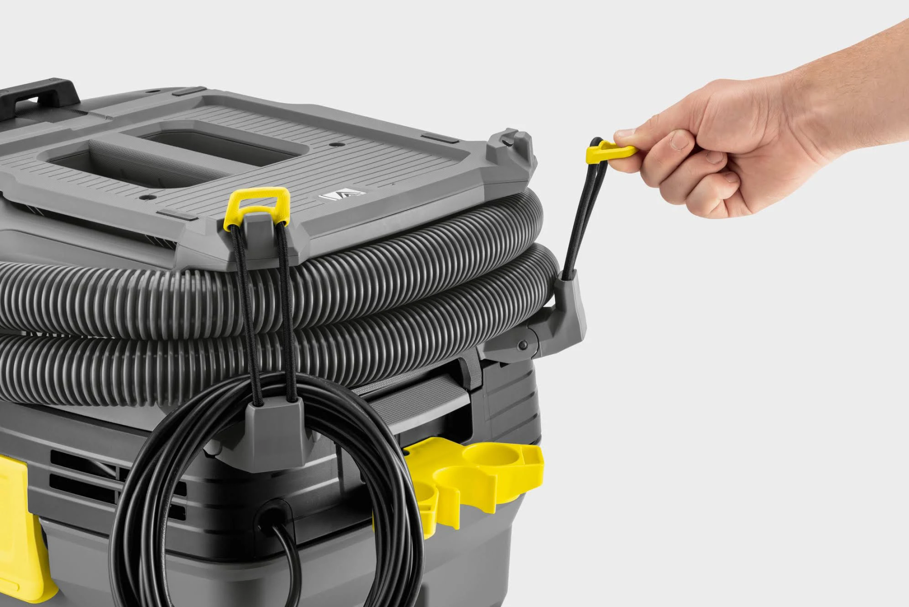 Ręka osoby pociąga za żółty uchwyt na szaro-czarnym odkurzaczu. Białe tło.