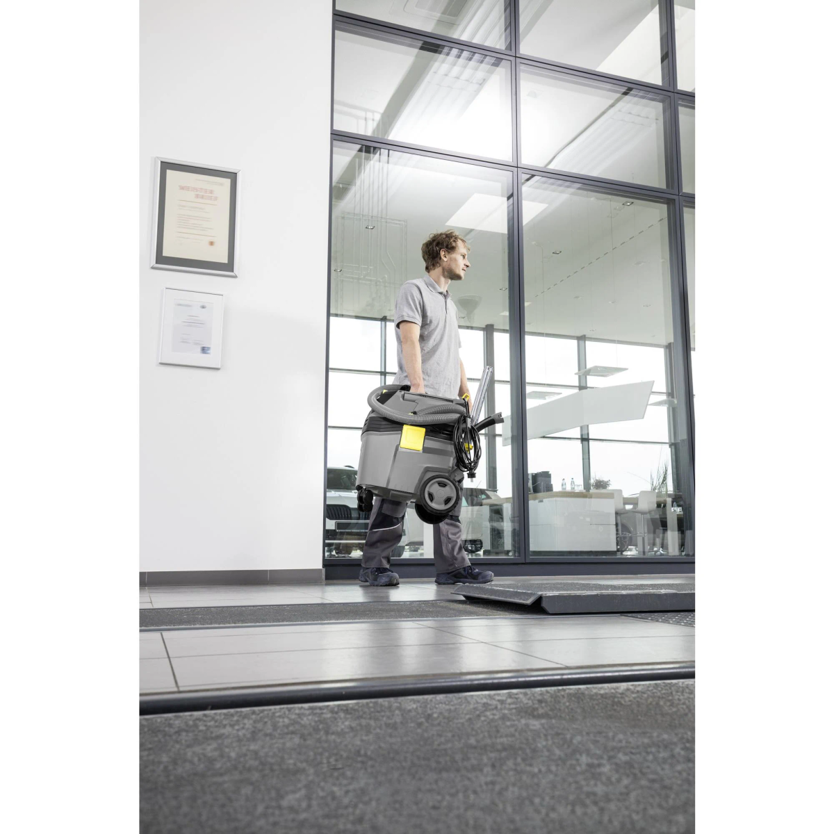 Mężczyzna idzie, niosąc maszynę do czyszczenia. Za nim szklana ściana.