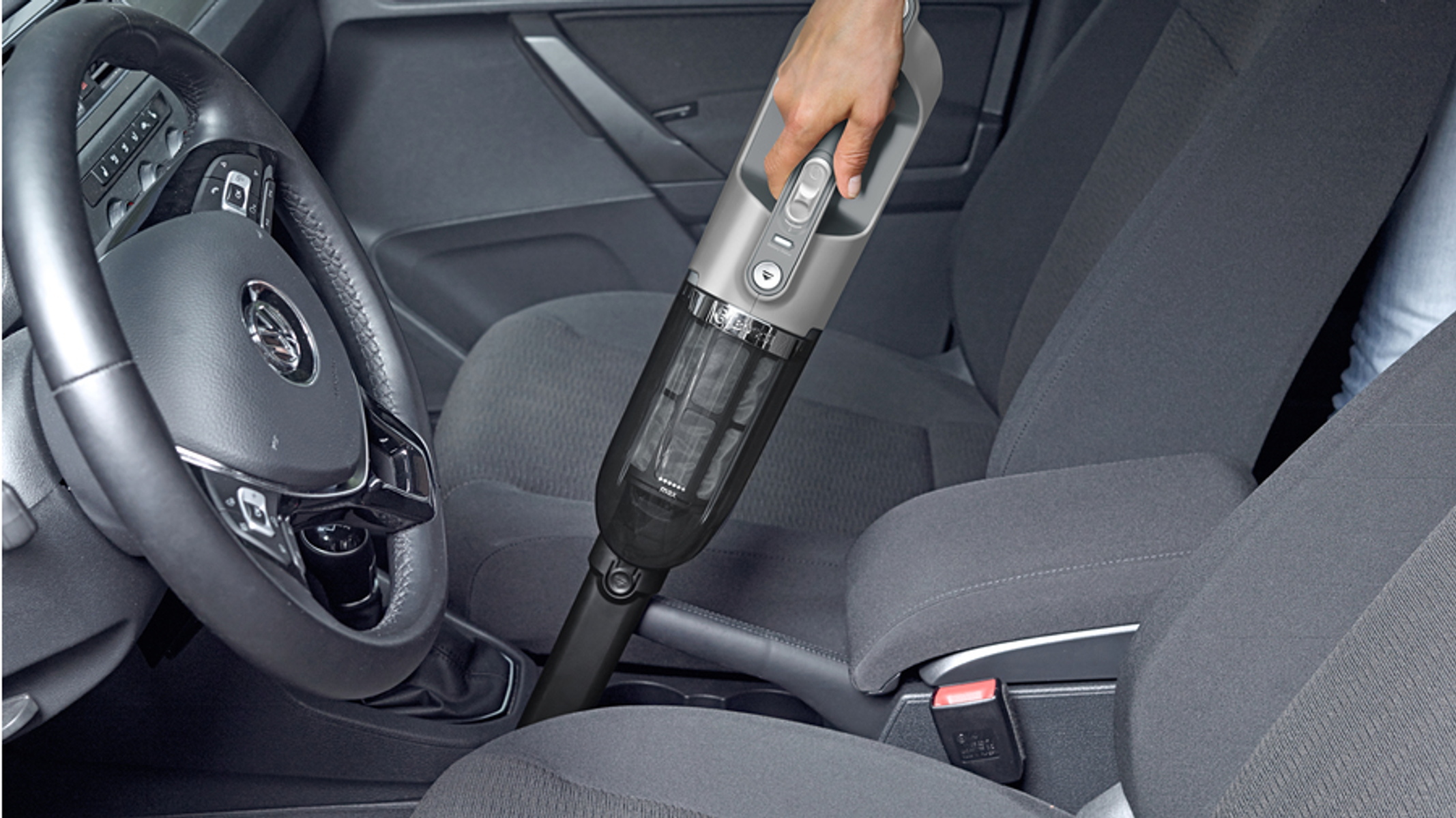 Person saugt Innenraum eines Autos. Ein schwarzer Staubsauger wird benutzt. Das Auto ist grau.