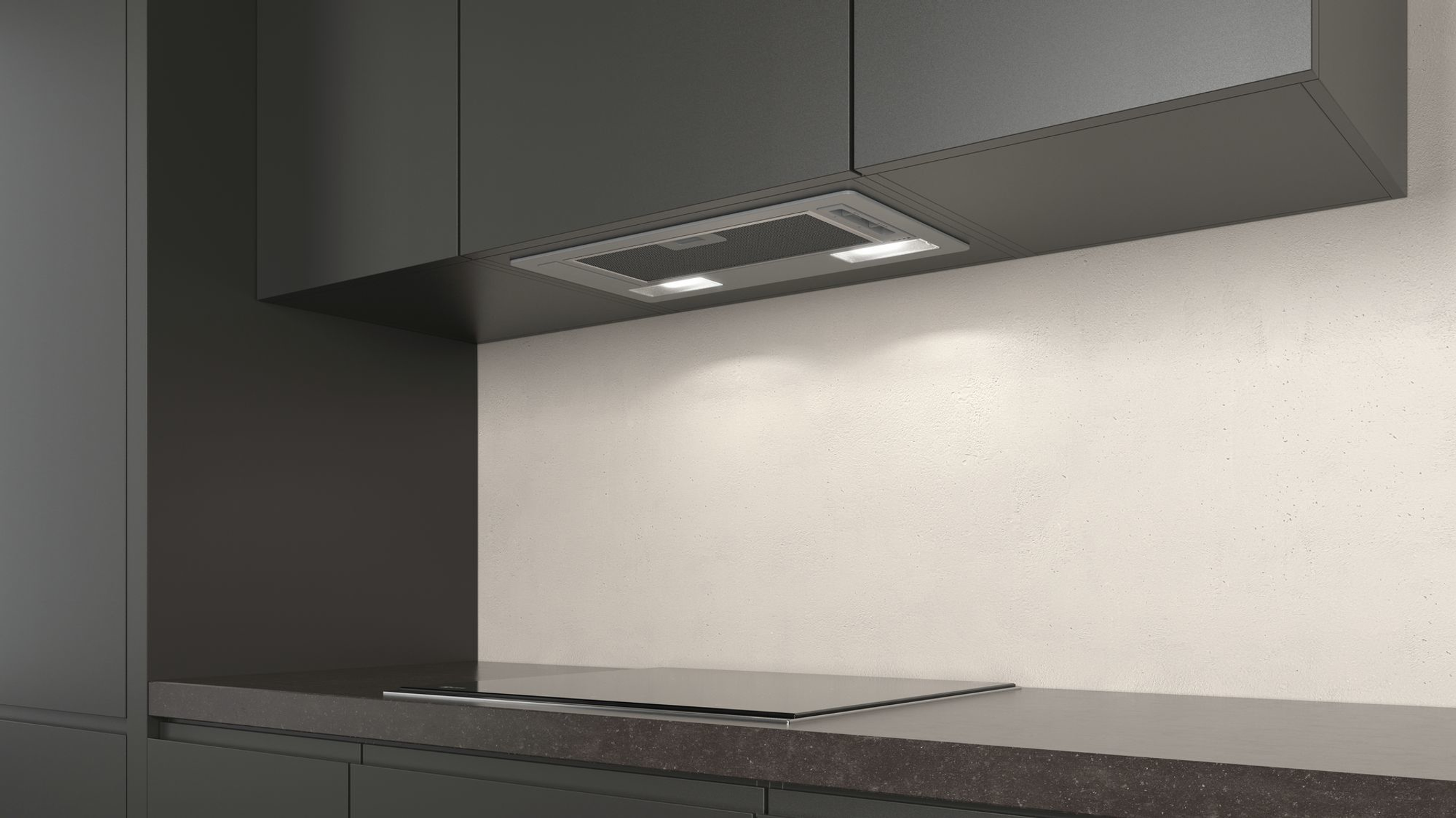 Cocina moderna con encimera y armarios oscuros. Una campana extractora empotrada tiene dos luces.