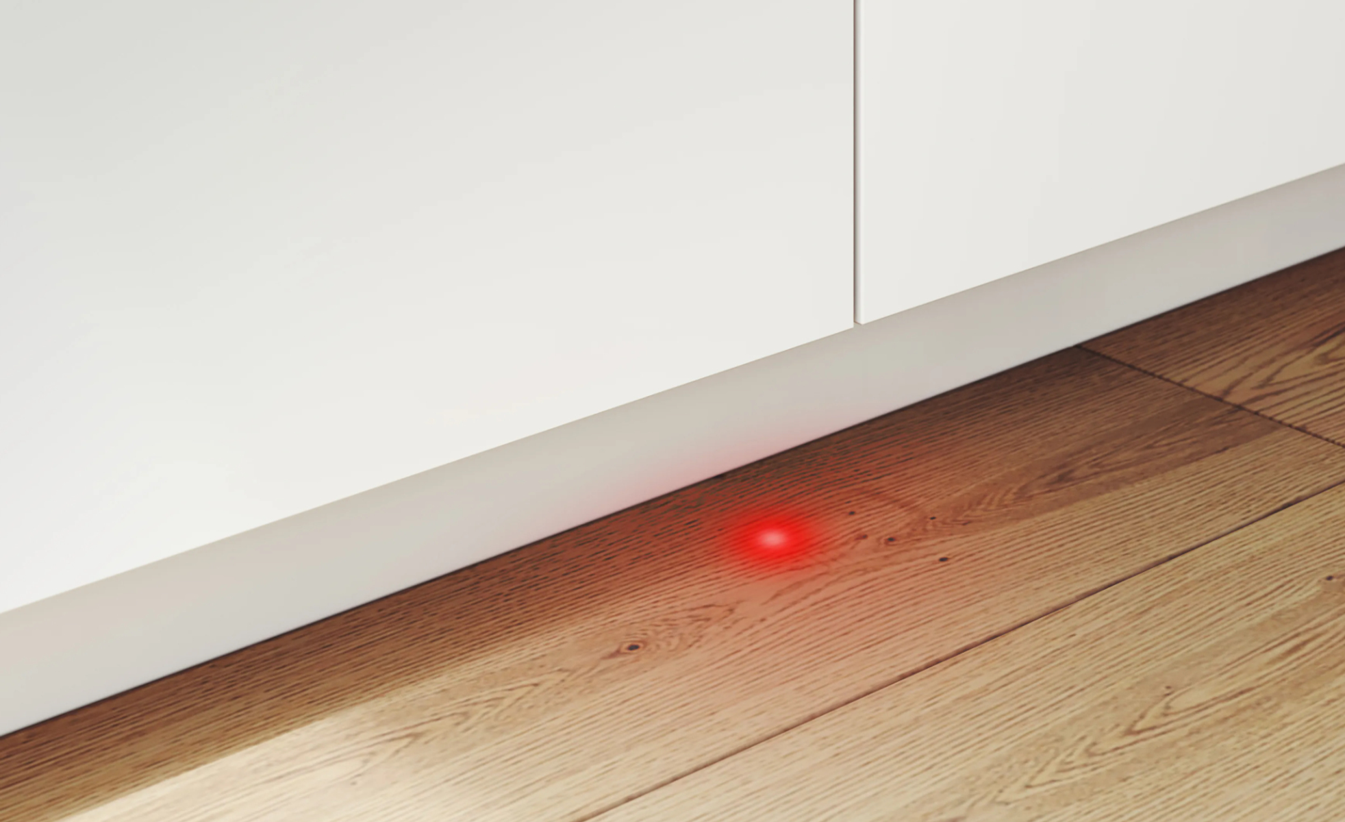 Rotes Licht, das auf einem Holzboden in der Nähe eines weißen Schranksockels leuchtet.