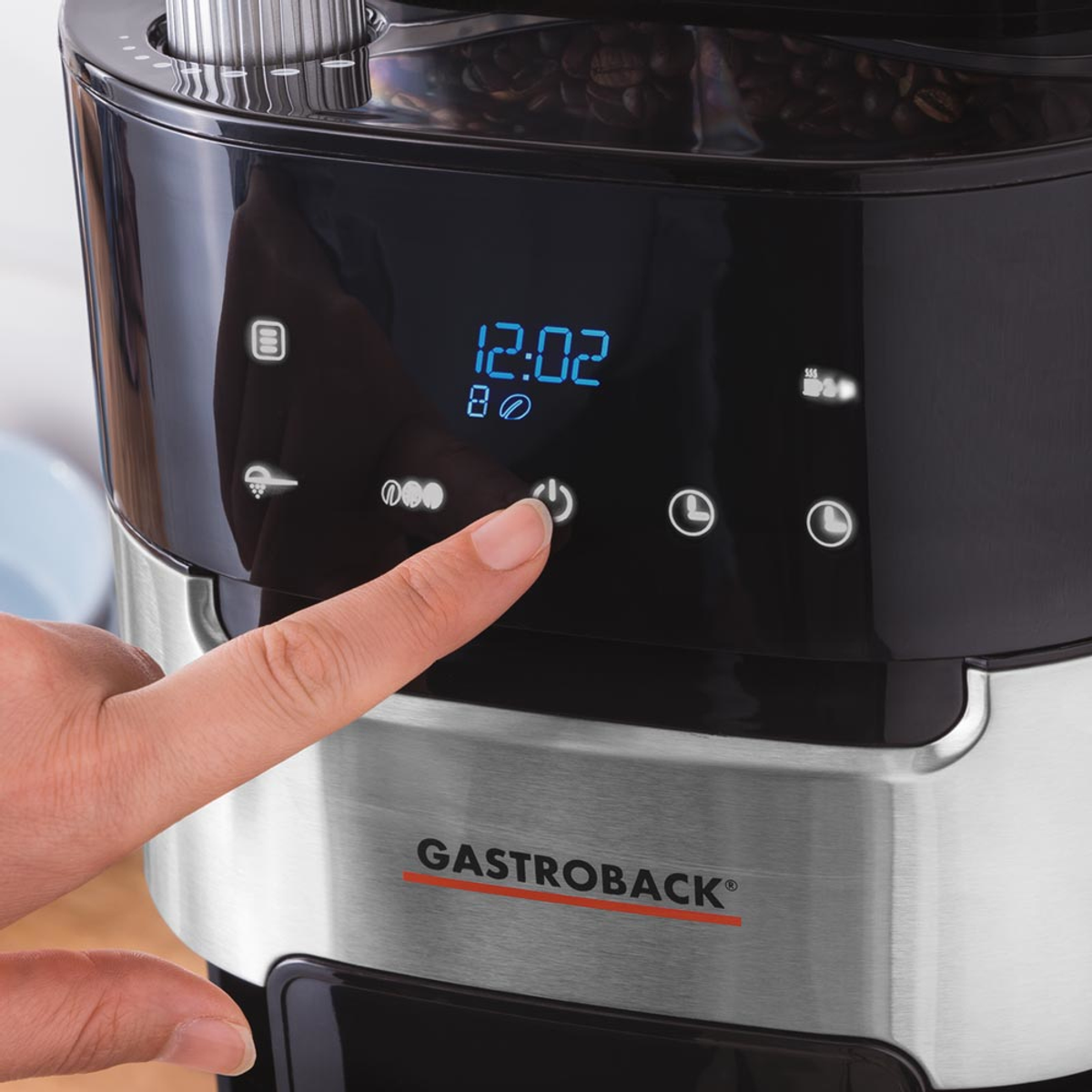 Il dito di una persona preme il pulsante di accensione su una caffettiera nera con display digitale.