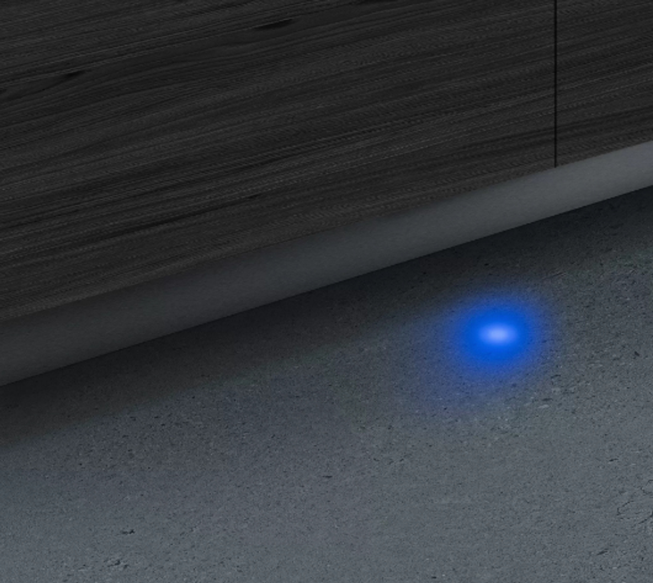 A blue light shining on a concrete floor, beneath a wooden structure.
