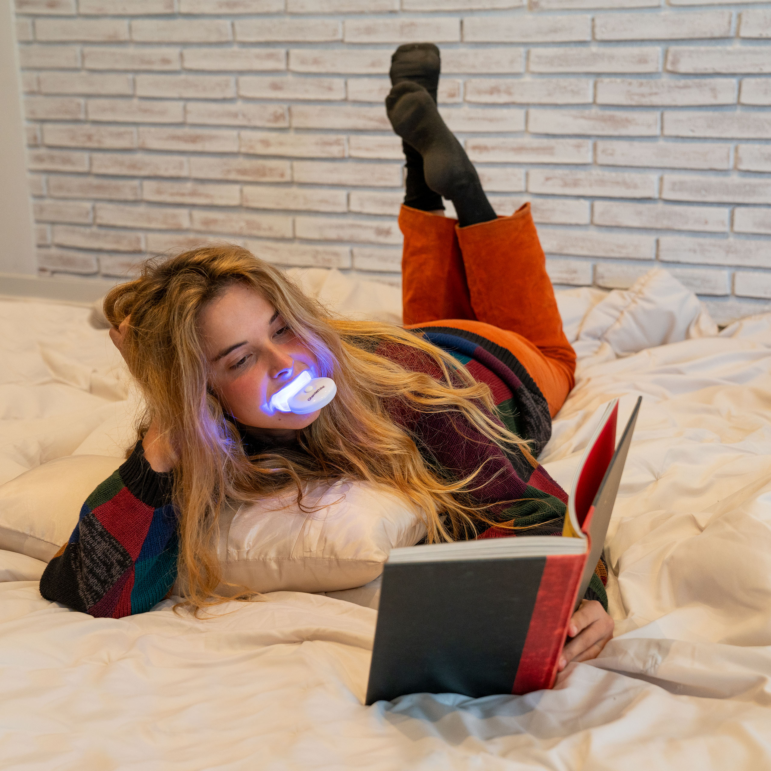 Mujer con protector bucal con luz azul acostada en la cama.