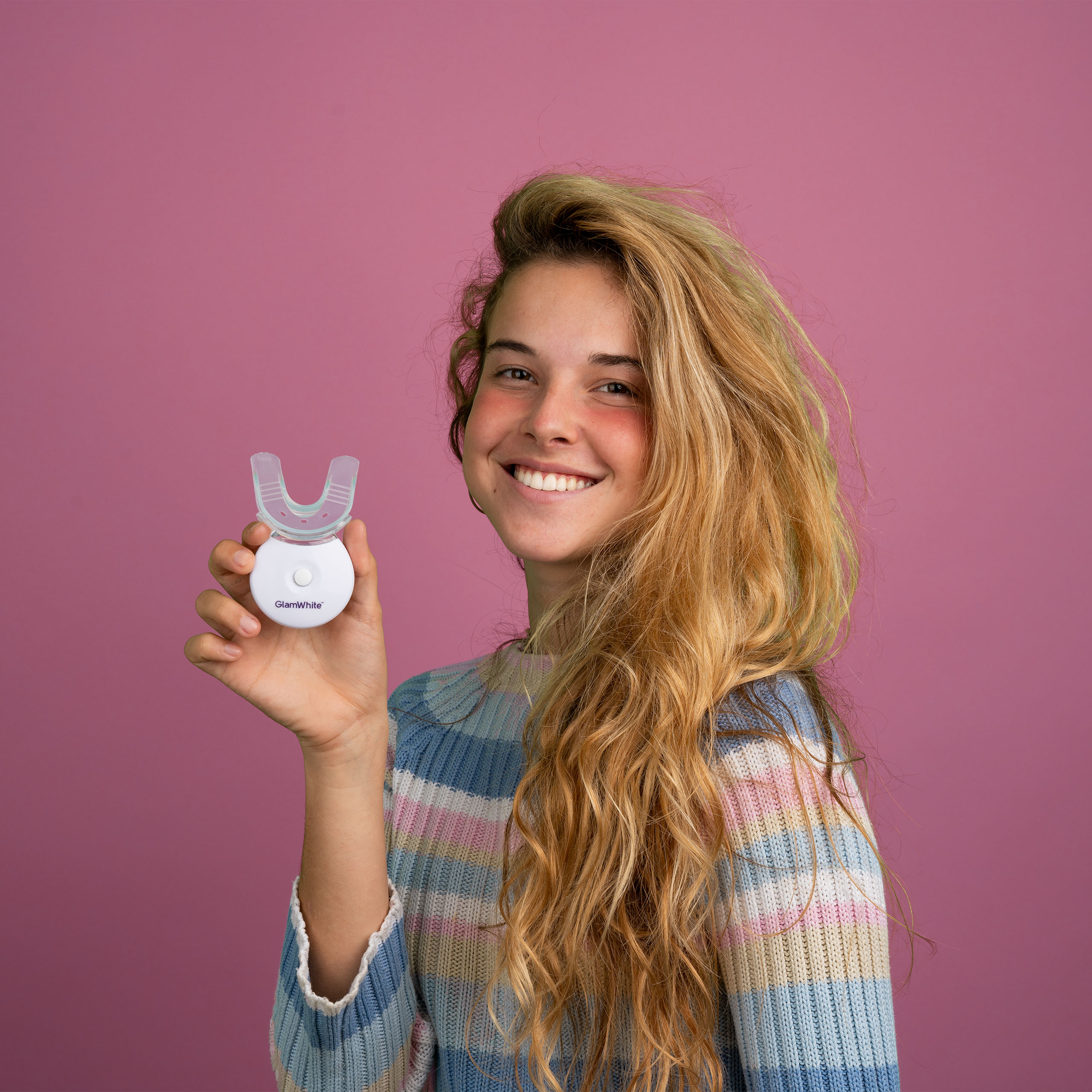 Mujer sosteniendo un dispositivo blanqueador dental blanco, sonriendo.