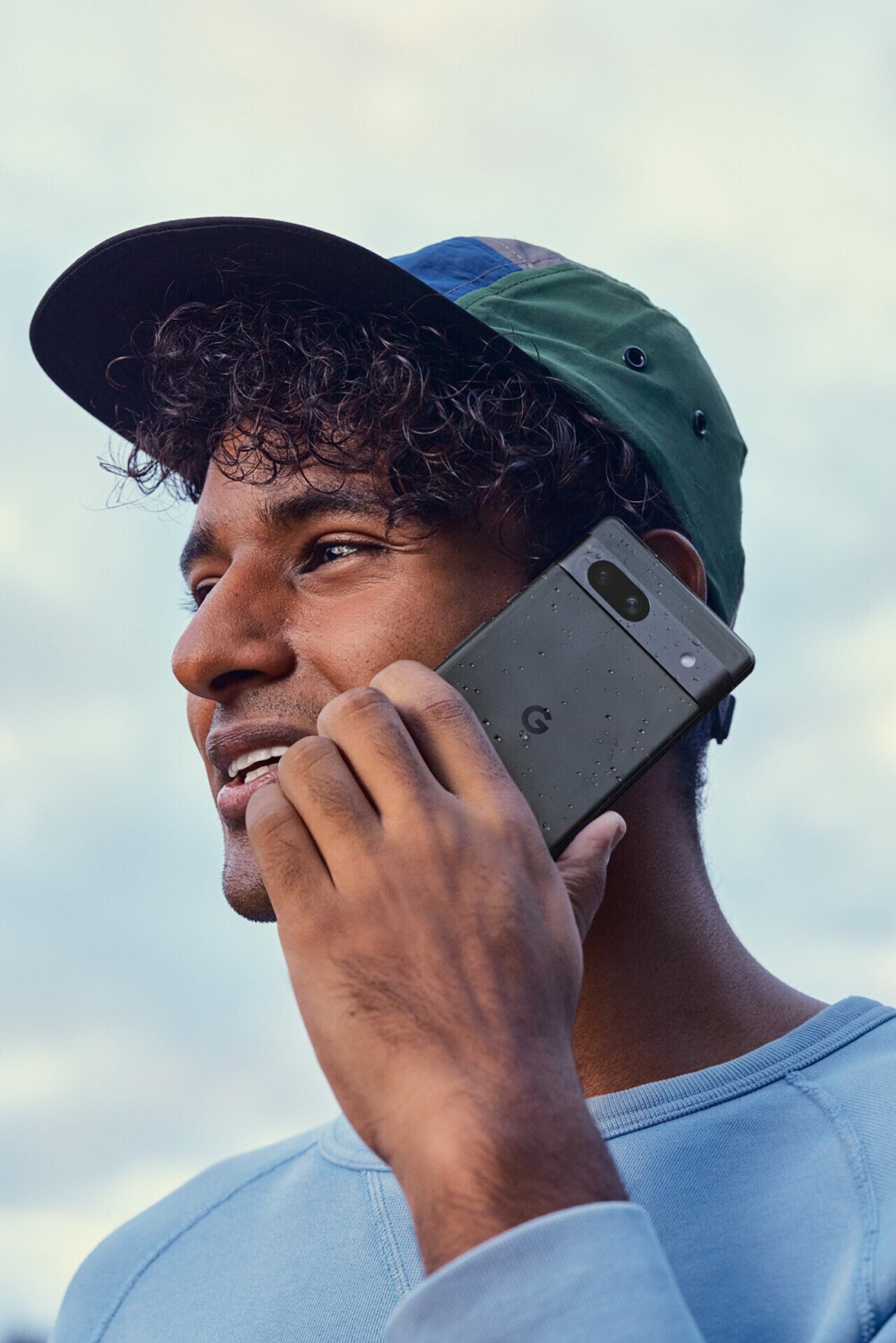 Mężczyzna rozmawia przez telefon. Ma na sobie czapkę i niebieską koszulę. Telefon jest czarny.