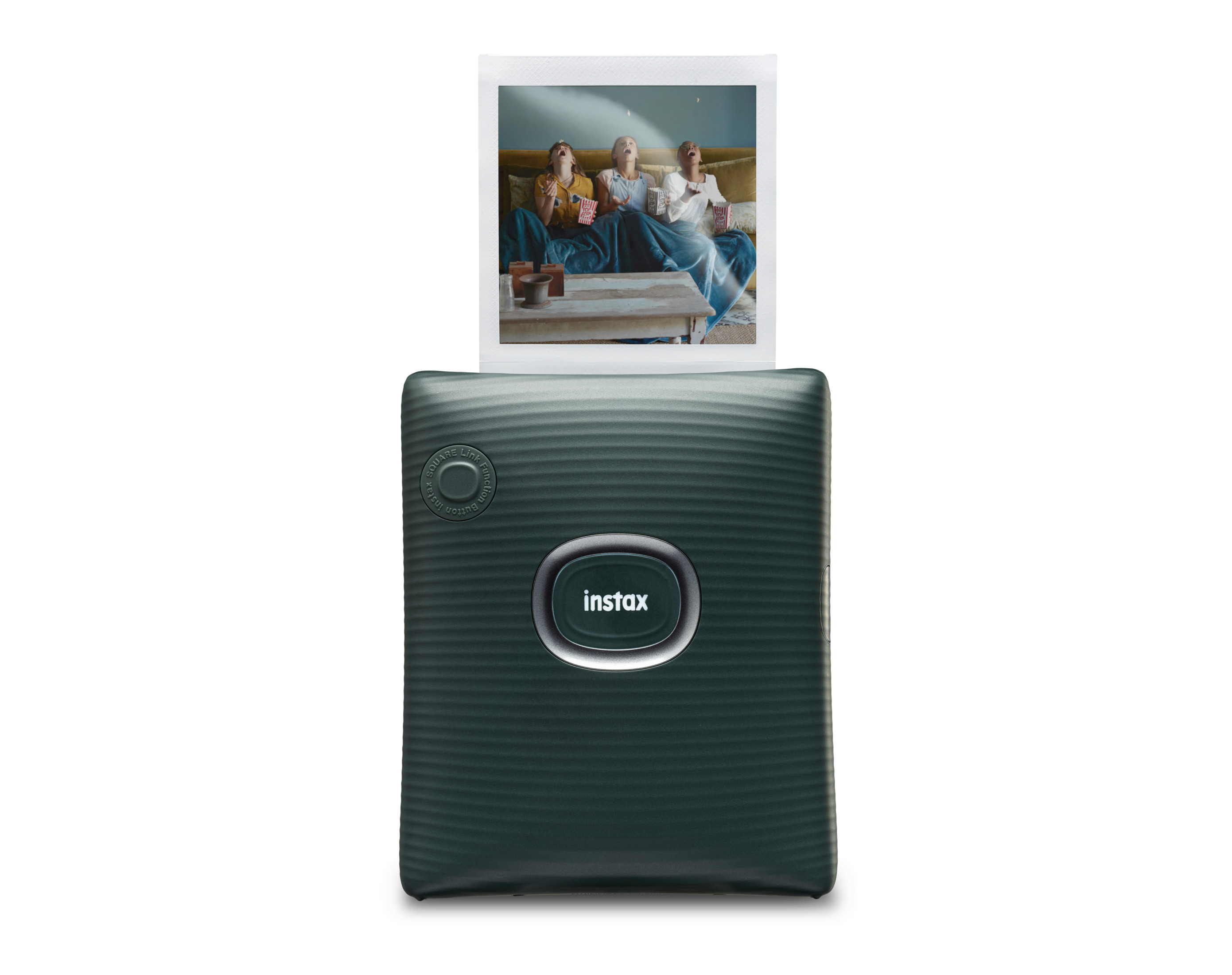 Una stampante Instax mostra una foto di tre donne che reagiscono a qualcosa. La stampante è verde scuro.