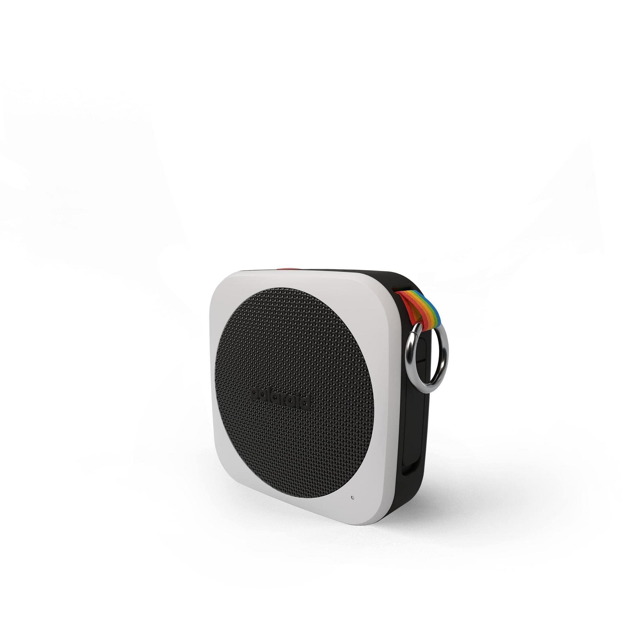 Kwadratowy biały głośnik z czarnym przodem z siatki, tęczowym paskiem i srebrnym pierścieniem.