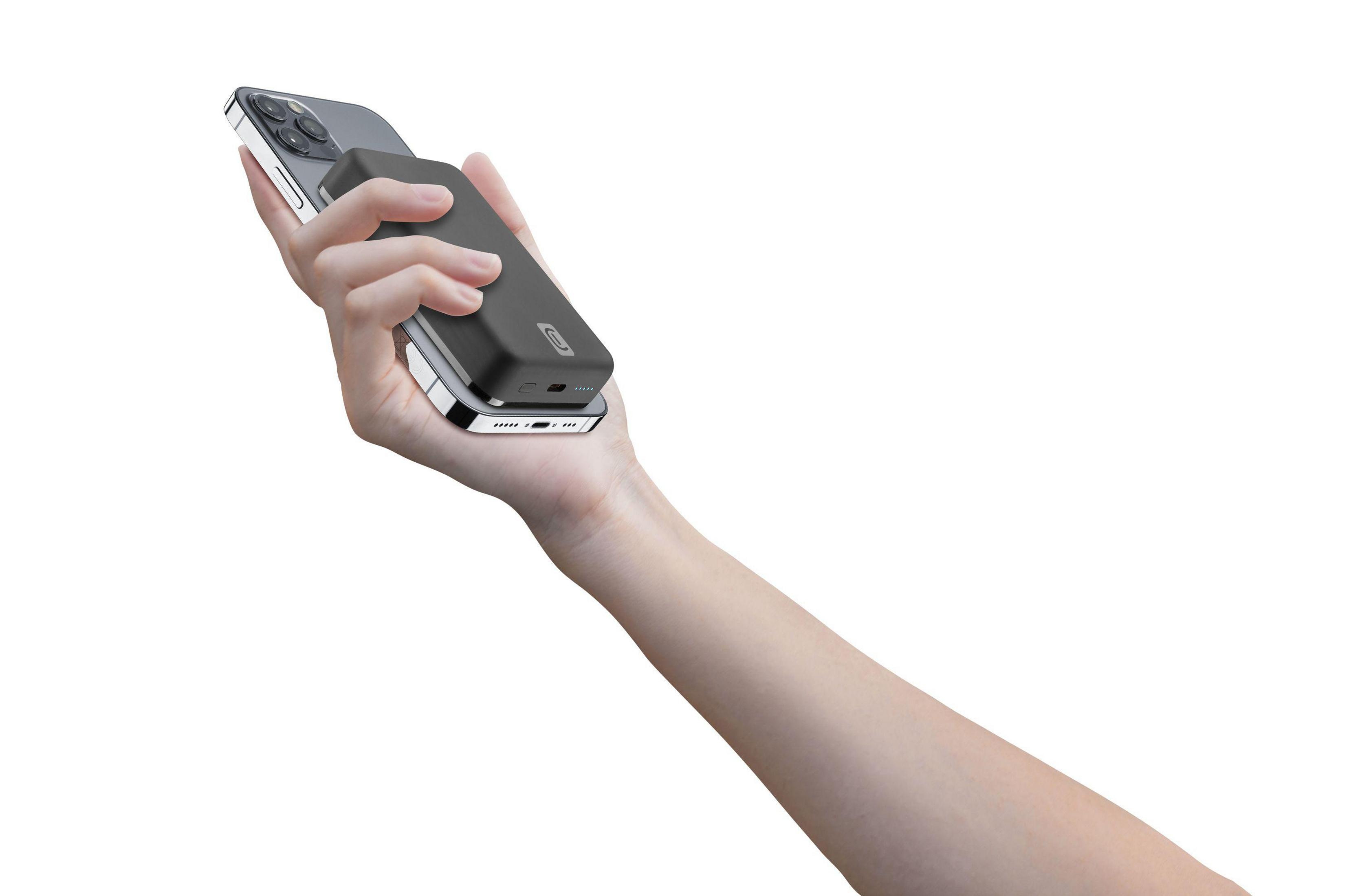Una mano sosteniendo un teléfono con un power bank. El teléfono es plateado, el power bank negro.