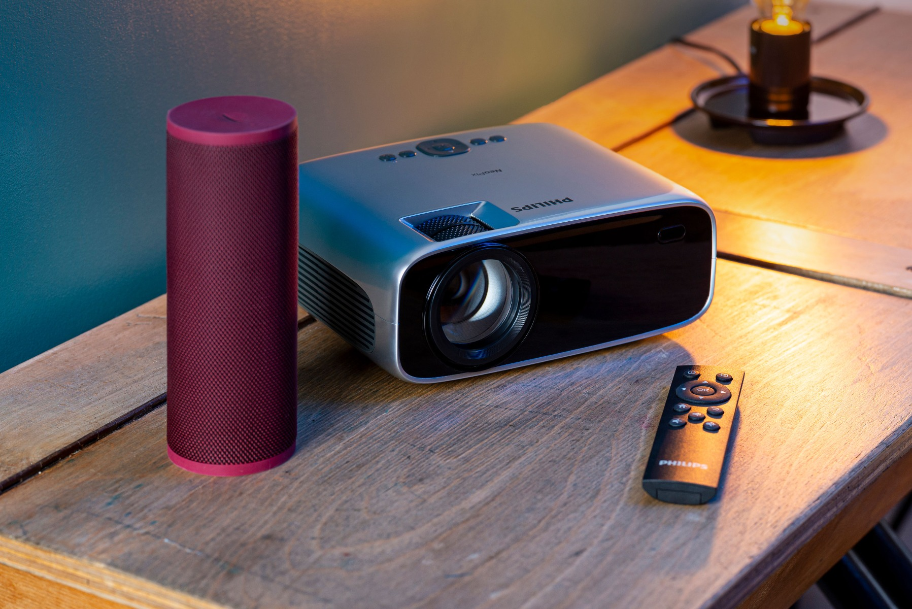 Projektor, głośnik i pilot na drewnianym stole. Ciemne tło.