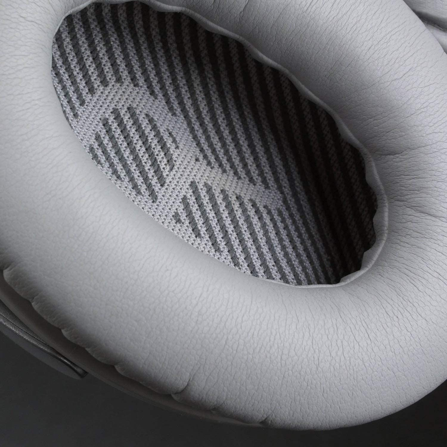 Zbliżenie jasnoszarej nausznicy słuchawek z niebiesko-czarnym paskowanym wnętrzem.