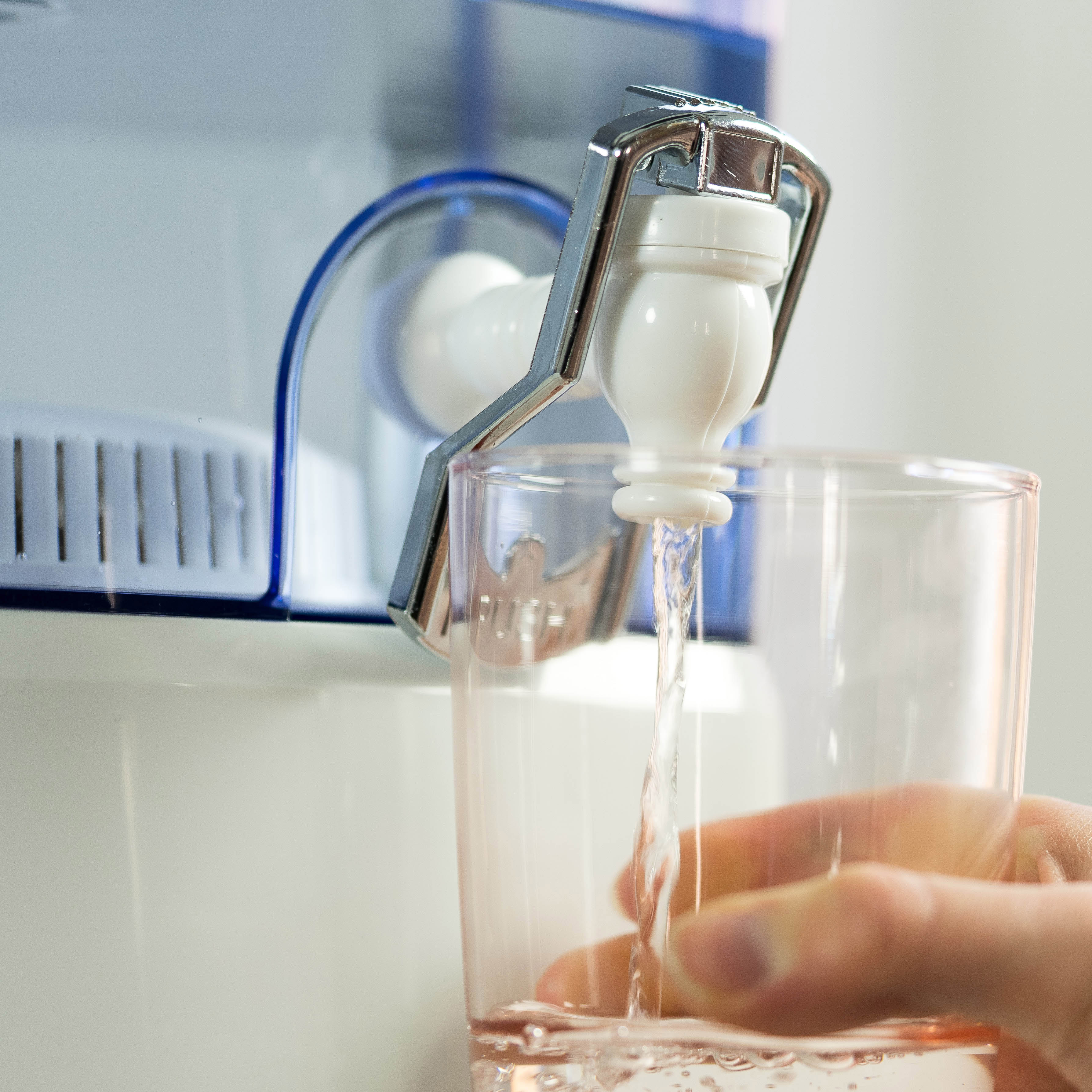 Una mano llenando un vaso con agua de un dispensador de agua.