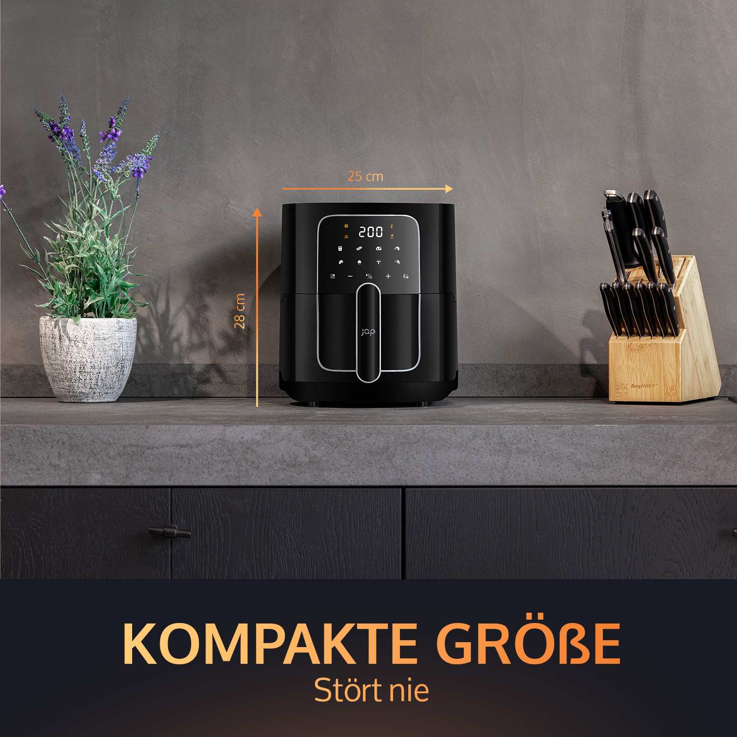 Black air fryer on a counter with a plant and knives. Dimensions are shown. Grey wall and black cabinets.
