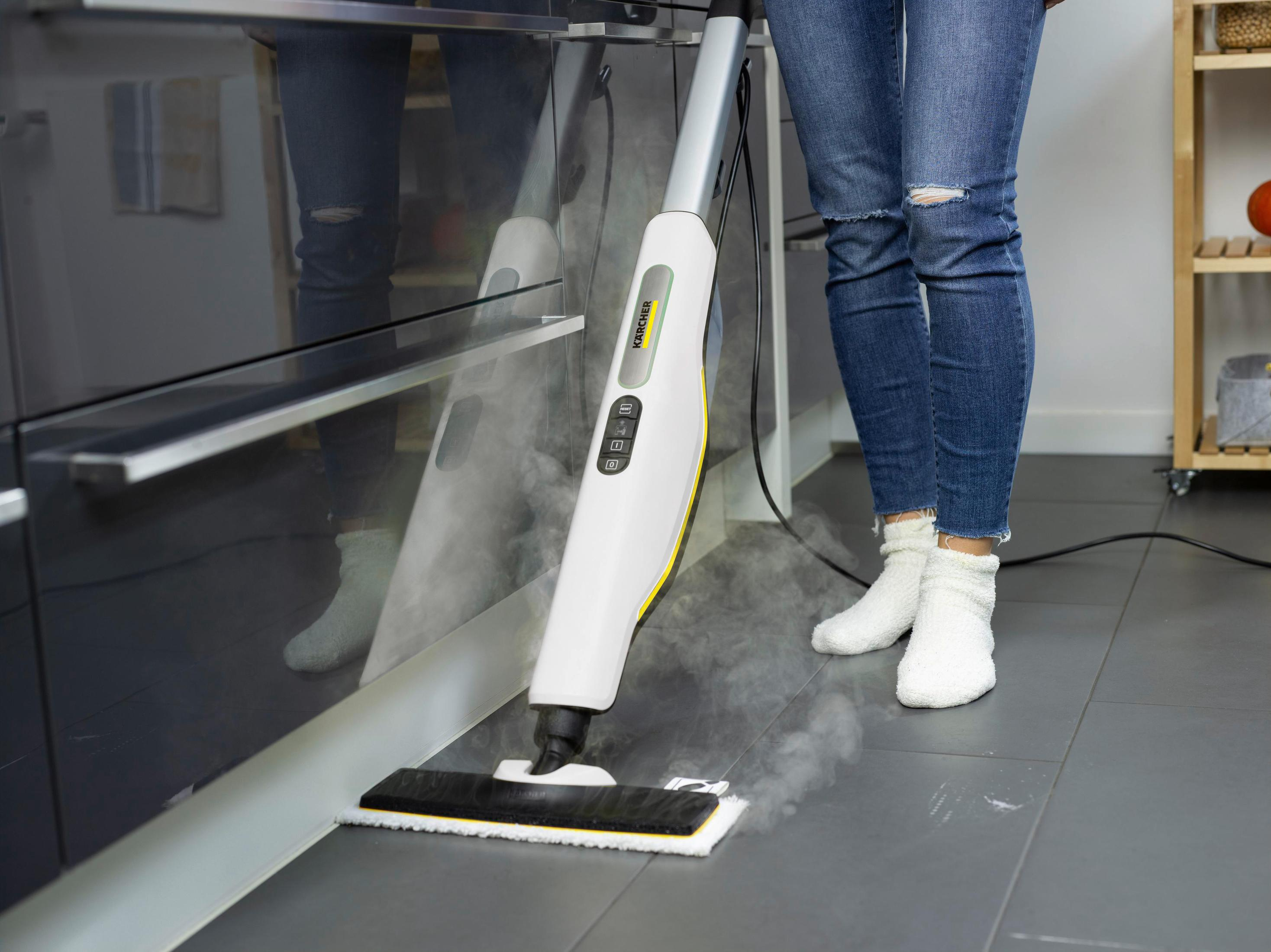 Kobieta czyści podłogę białym mopem parowym. Szara podłoga. Tło kuchenne.