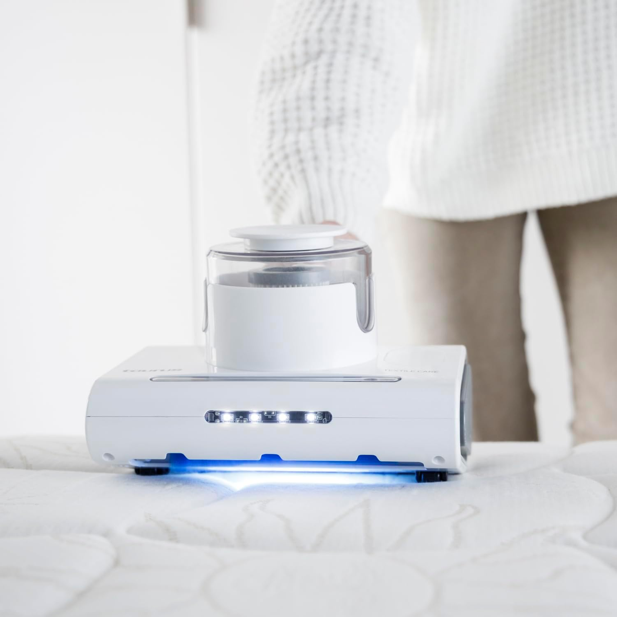 Biały odkurzacz z przezroczystym wierzchem na białym materacu.