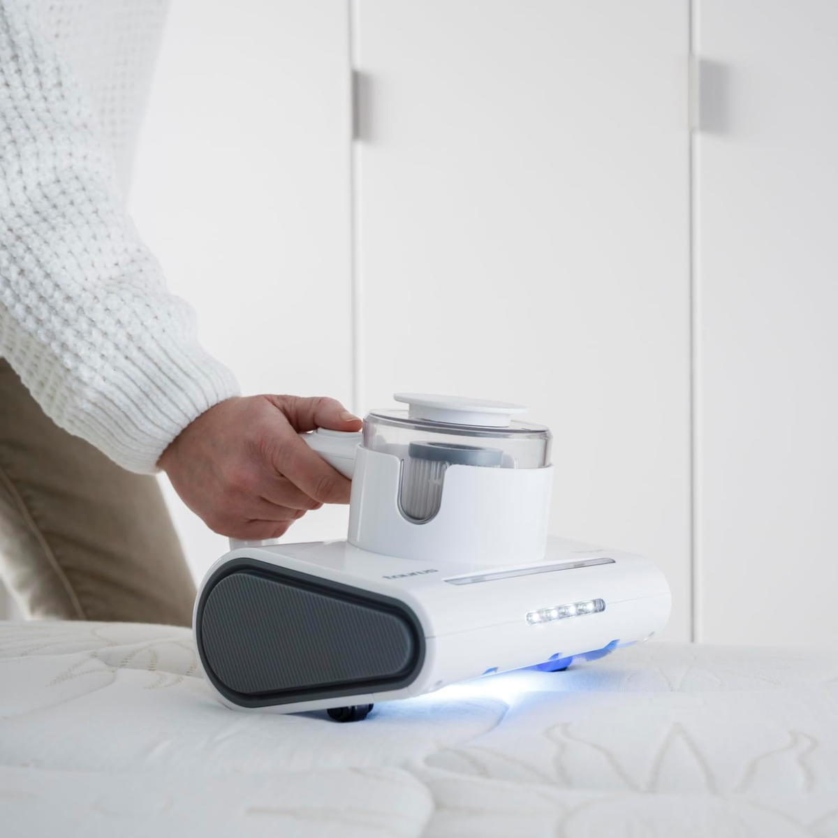 Osoba używa białego odkurzacza bezprzewodowego do czyszczenia białego materaca.