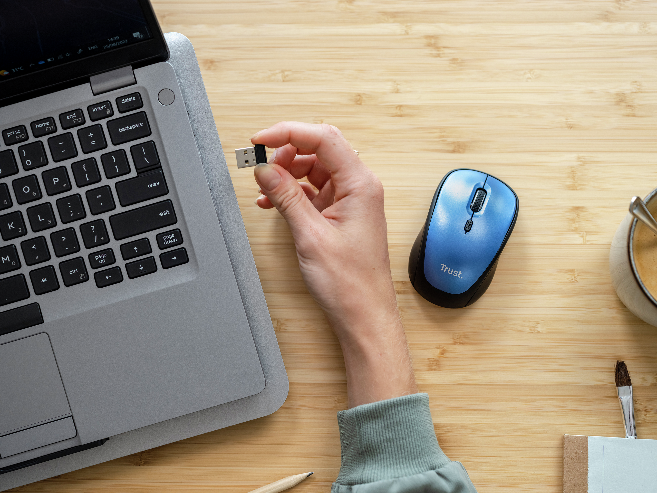 Ręka trzymająca USB, laptop, niebieską mysz i filiżankę kawy.