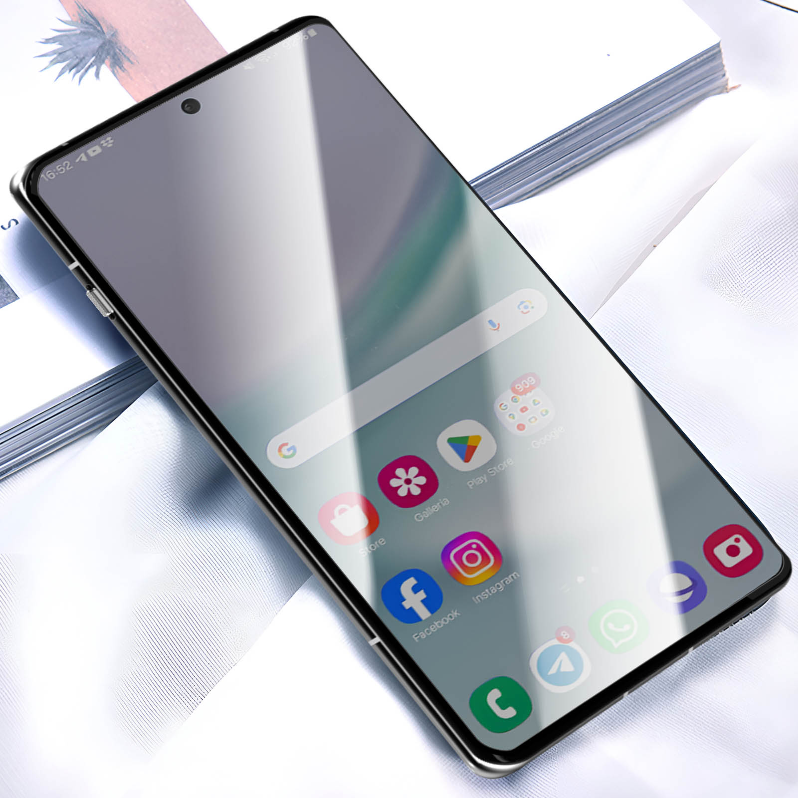 Uno smartphone mostra la sua schermata iniziale. Sono visibili le icone di app come Store, Facebook e Instagram. Il telefono è appoggiato su una superficie bianca.