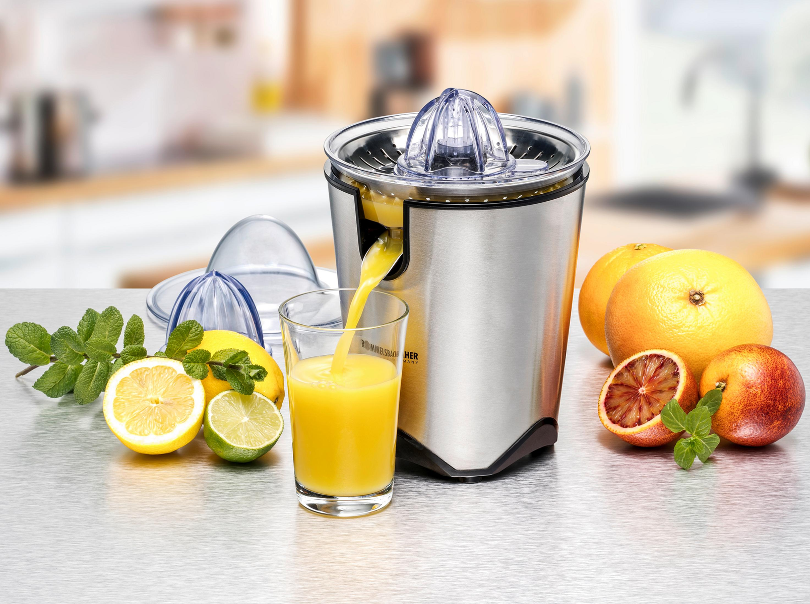 Juicer with a glass of juice, oranges, and lemons on a table. The background is blurred.