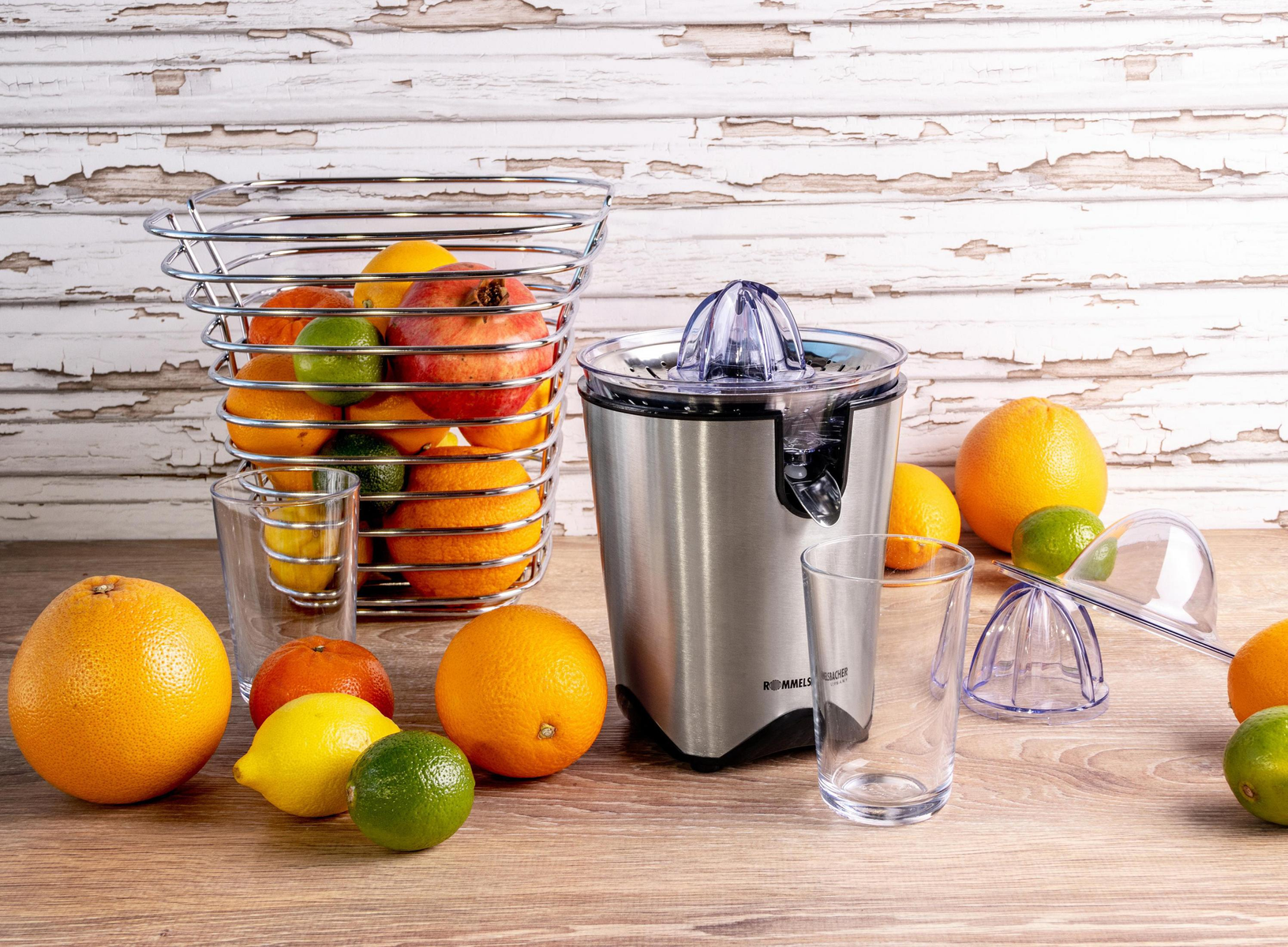 Citrus juicer with oranges, lemons, and limes, and a basket of fruit. Two glasses are in front.