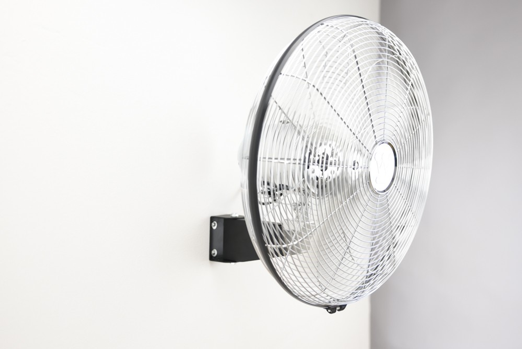 Wandventilator, silberne Blätter in einem schwarzen Rahmen, an einer weißen Wand montiert.