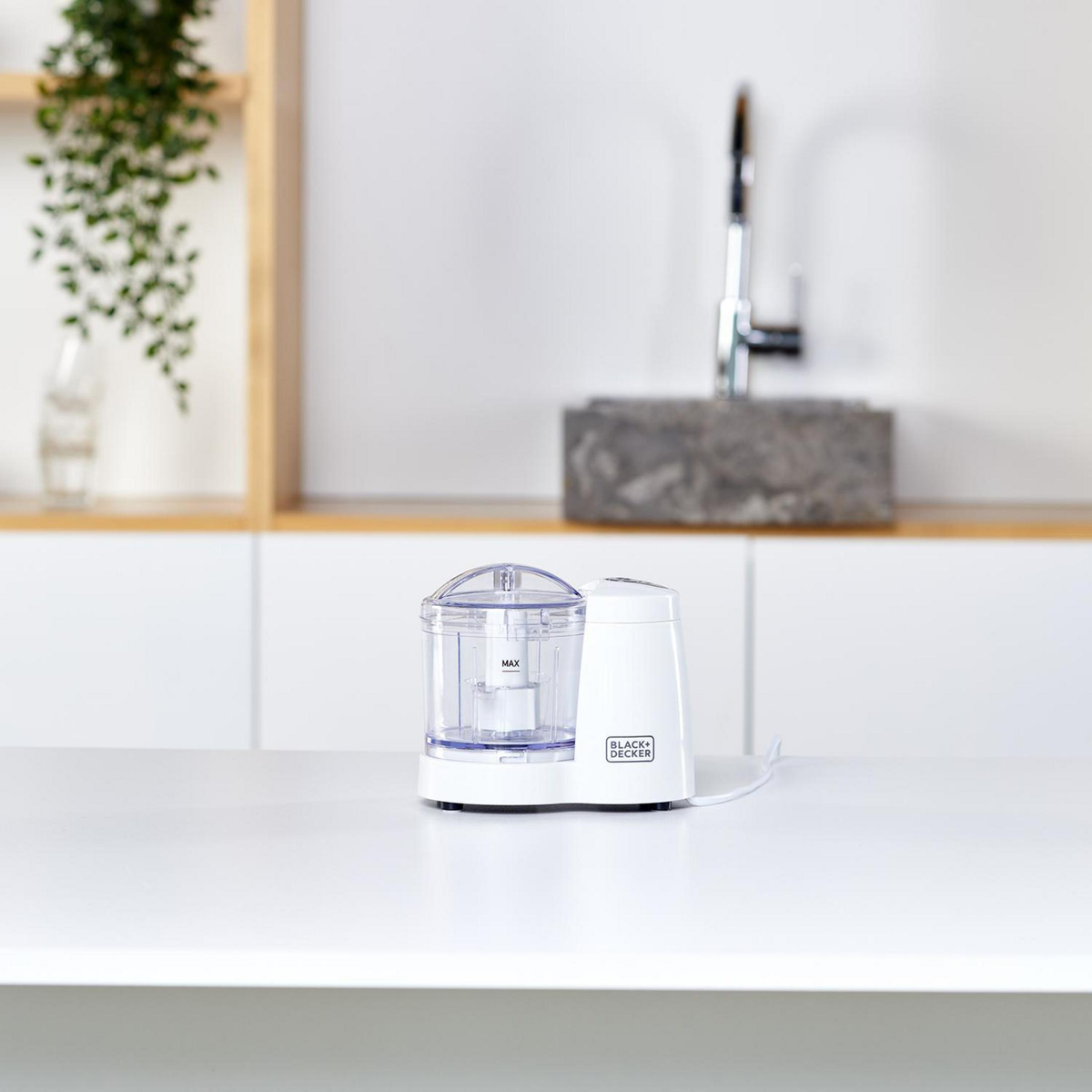 Mini tritatutto Black+Decker bianco su tavolo bianco, verde e lavandino sullo sfondo.