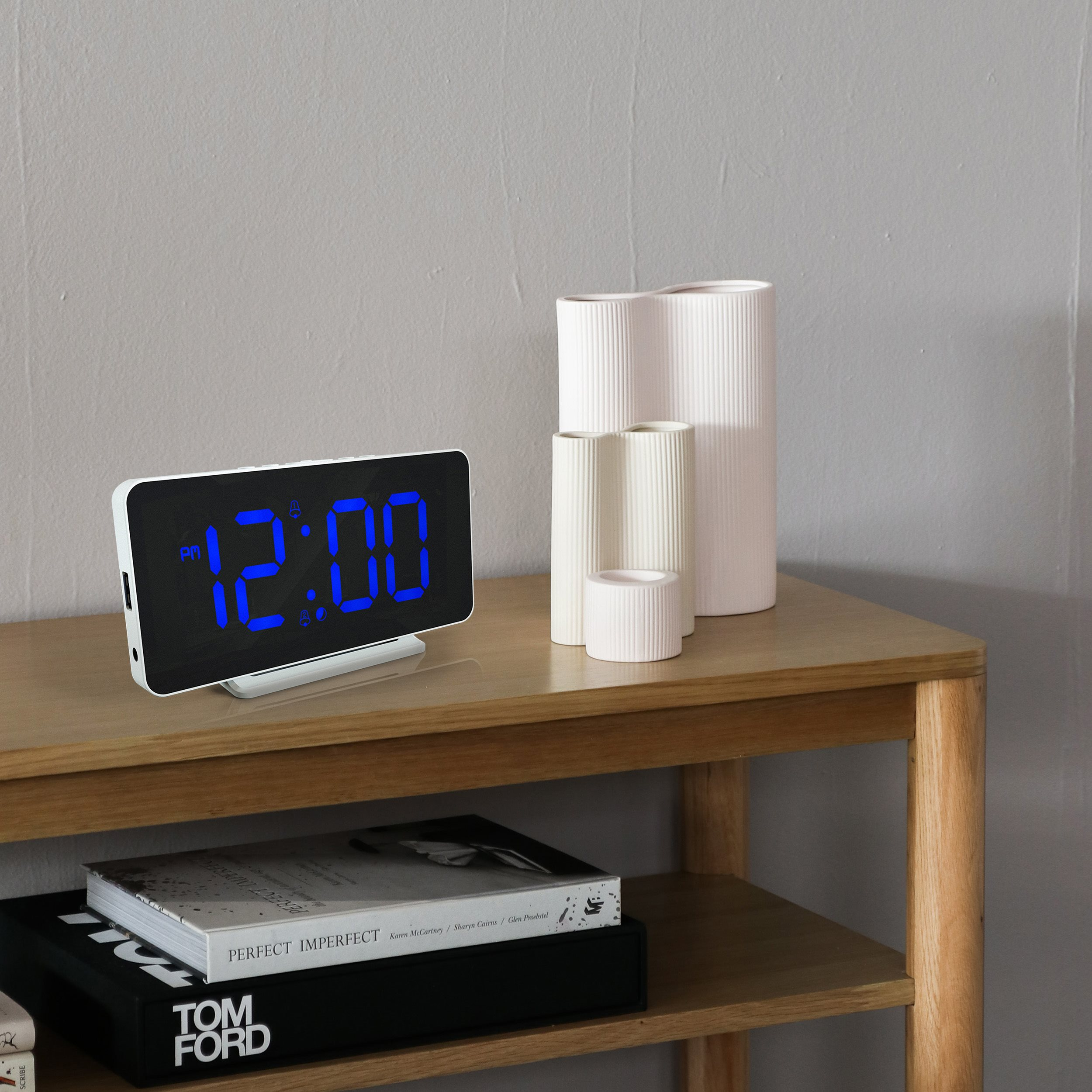 Digital clock displays 12:00. Vases stand on a wooden table. Books are below the table.