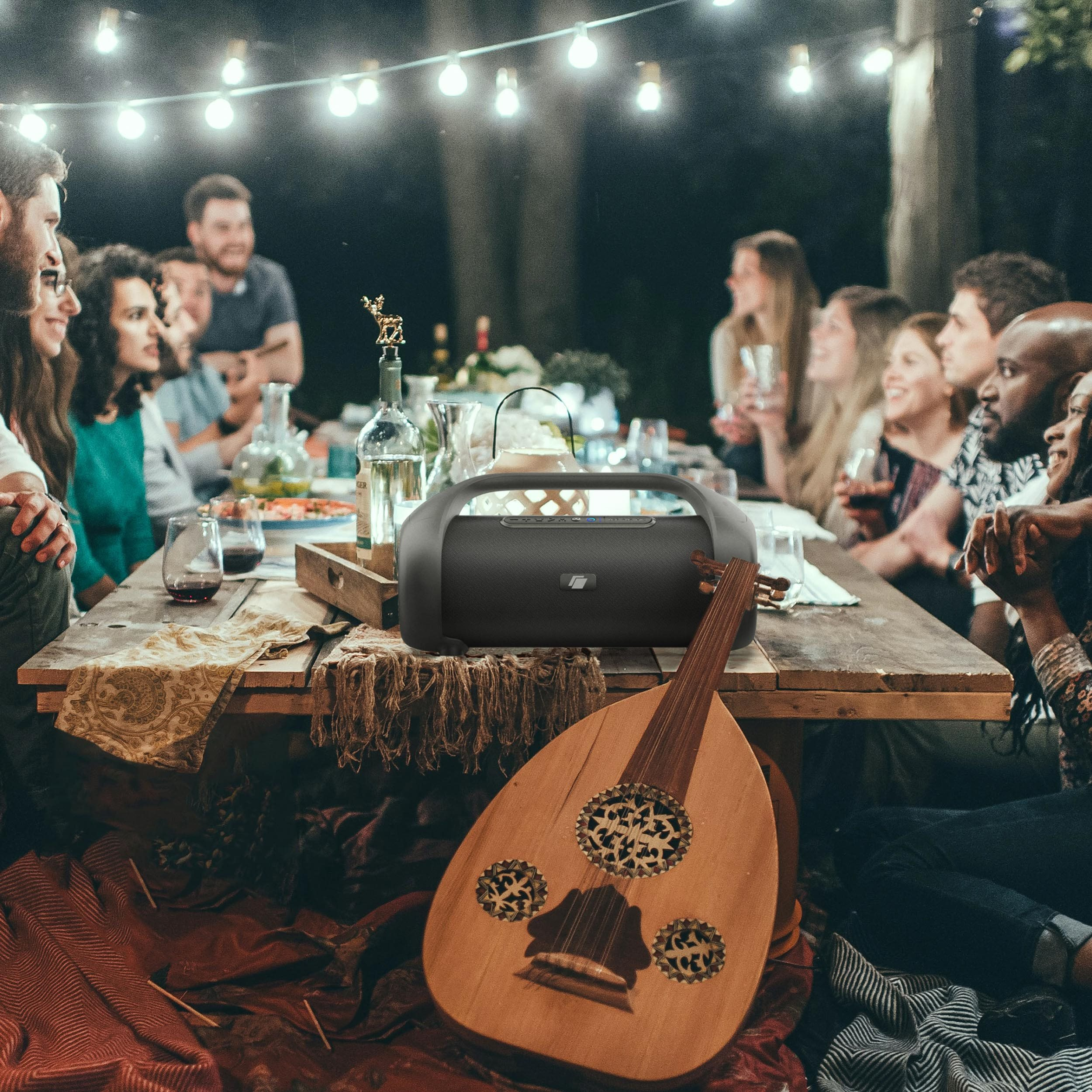 Menschen versammeln sich um einen Tisch mit Essen, einem Lautsprecher und einer Oud bei Nacht.