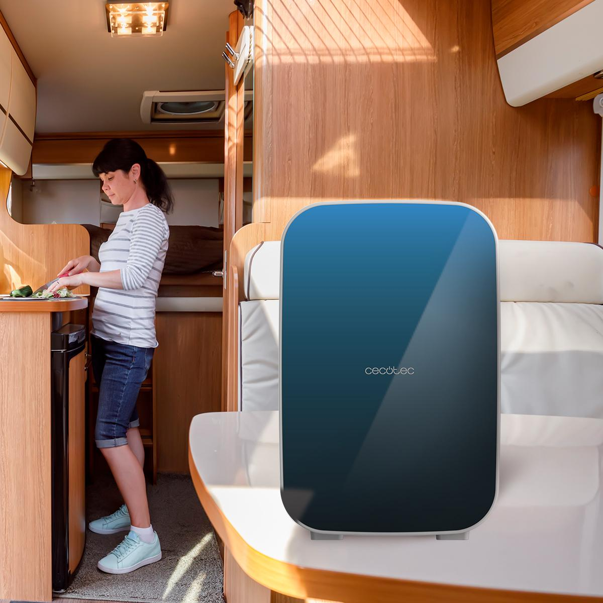 Una mujer cortando verduras en una caravana con un electrodoméstico azul y negro.
