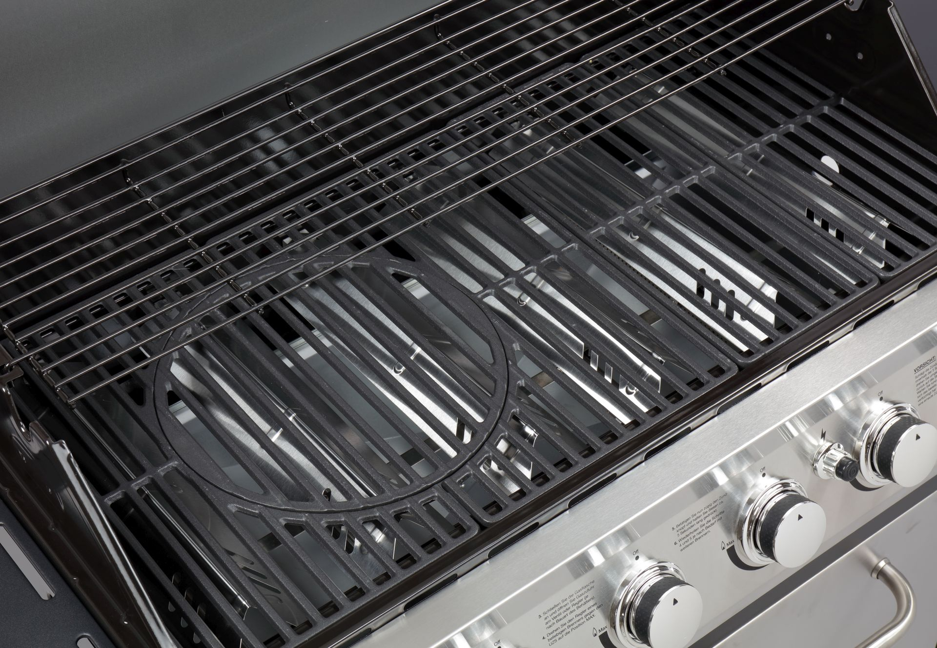 Nahaufnahme eines Grills mit schwarzen Rosten. Edelstahlbasis mit sichtbaren Bedienelementen.