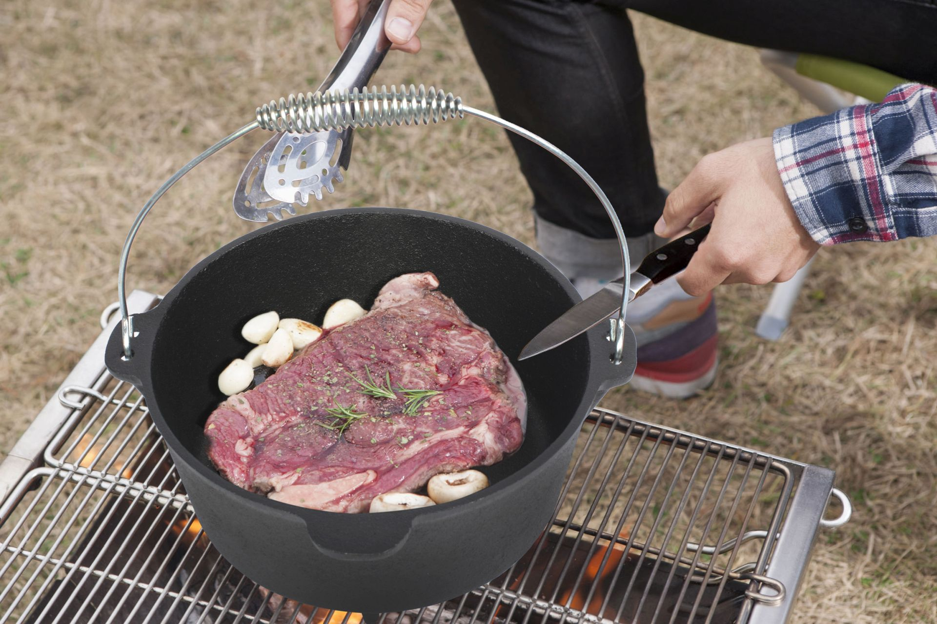 Fleisch in einem schwarzen Topf auf einem Grill. Knoblauch und Rosmarin auf dem Fleisch. Person kocht.