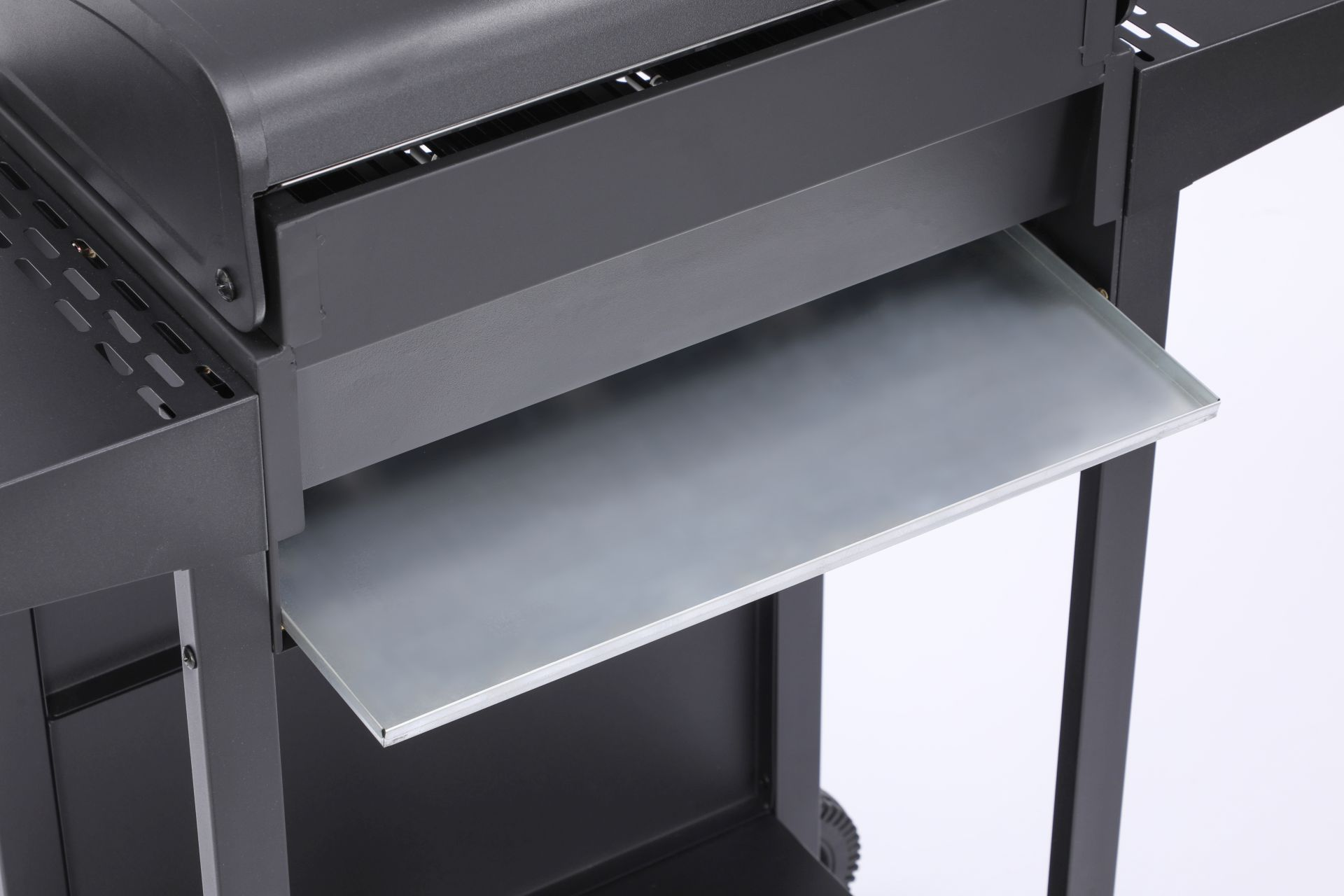 Nahaufnahme eines schwarzen Grills. Ein Metalltablett wird herausgezogen. Weißer Hintergrund.