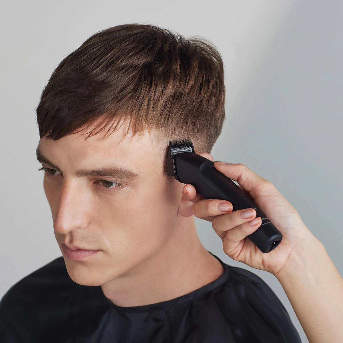 Una persona si taglia i capelli con un tagliacapelli nero.