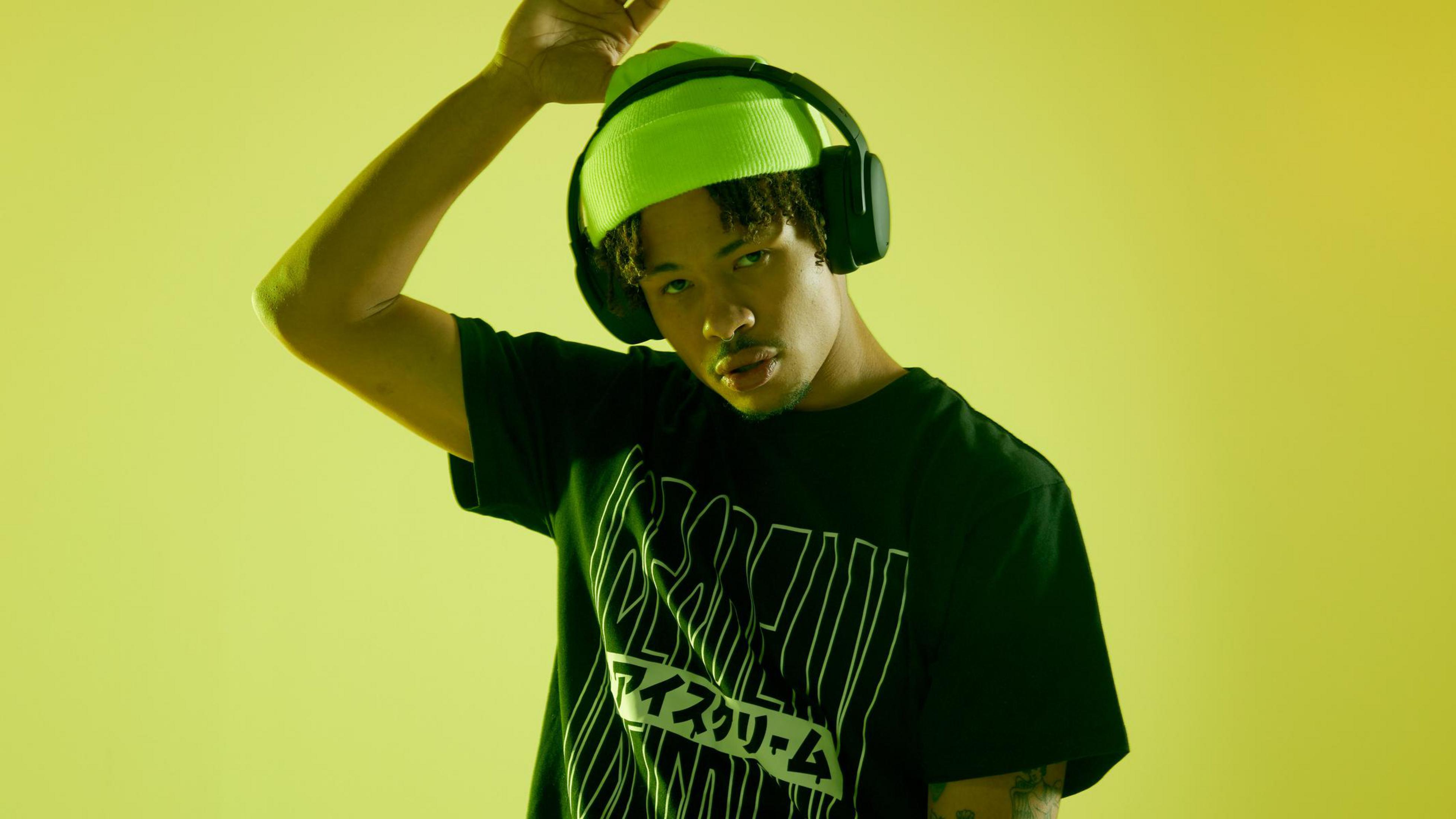 Młody mężczyzna ze słuchawkami i czapce pozuje na żółtym tle.