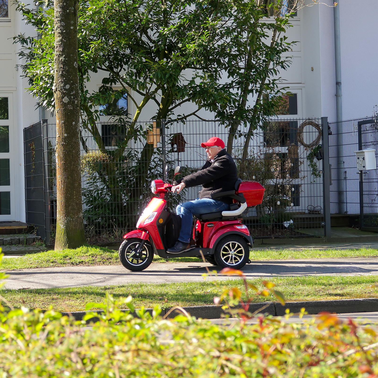 Eine Person fährt an einem sonnigen Tag mit einem roten Mobilitätsroller.