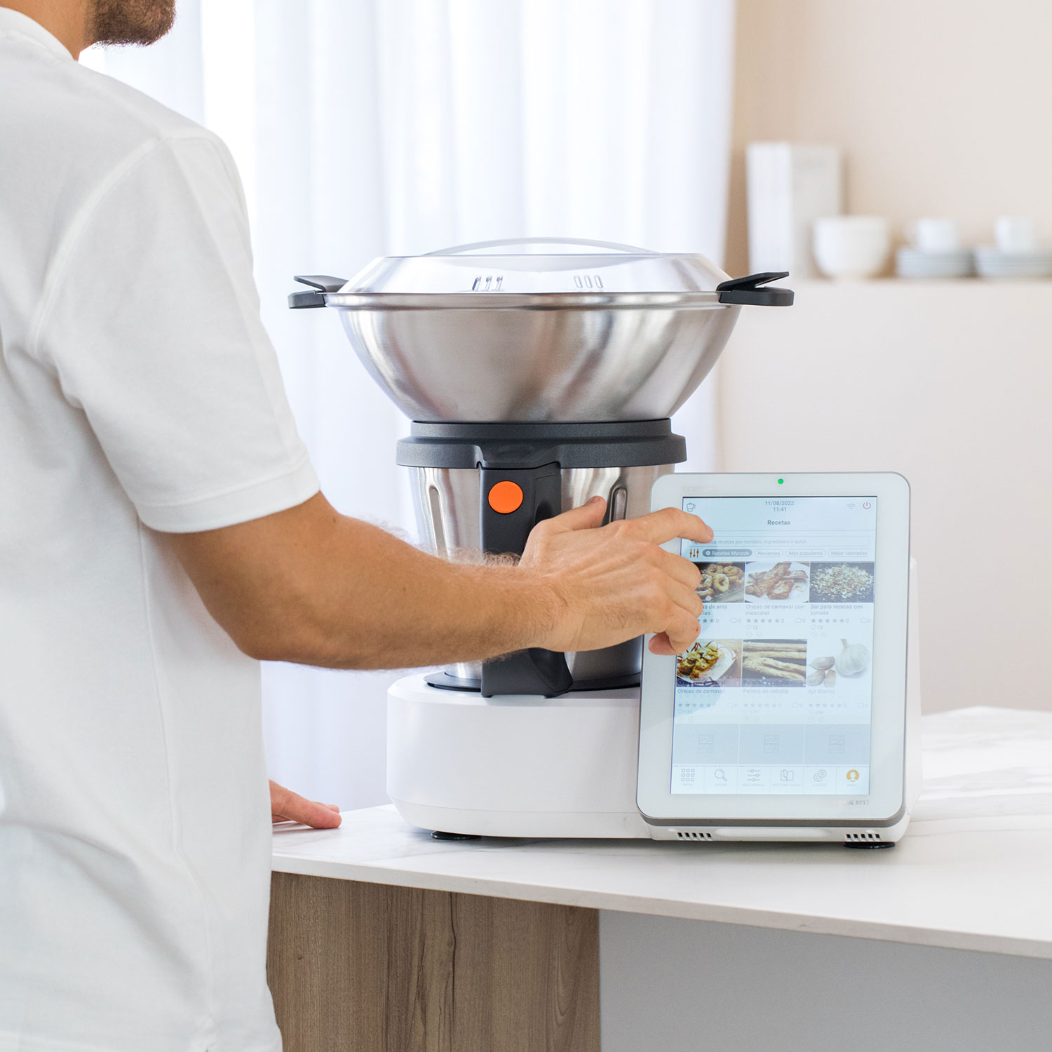 Una persona usa una tableta junto a un electrodoméstico de cocina plateado. La pantalla muestra una aplicación de recetas.