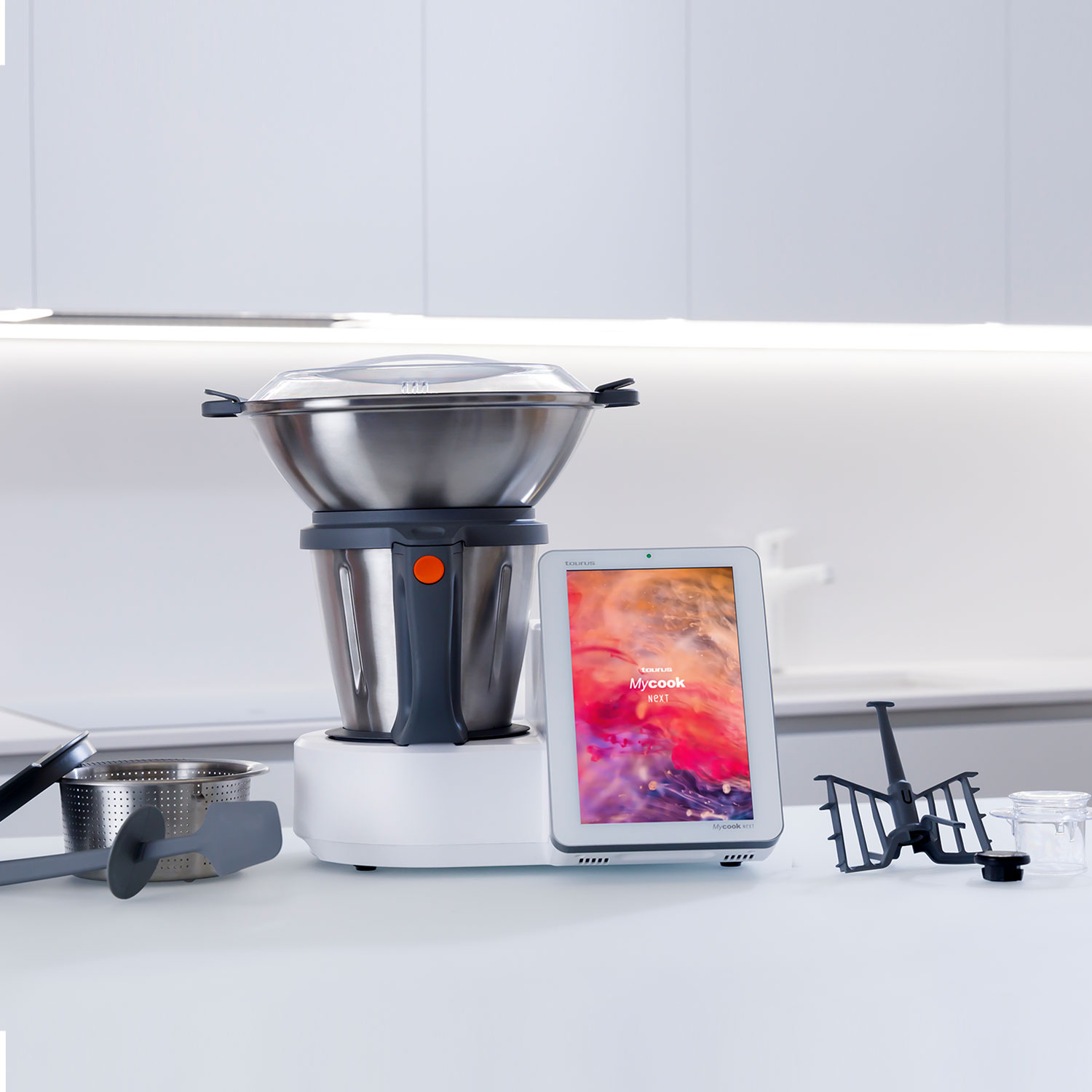 Un electrodoméstico de cocina Mycook con pantalla digital, utensilios de cocina y superficie blanca.